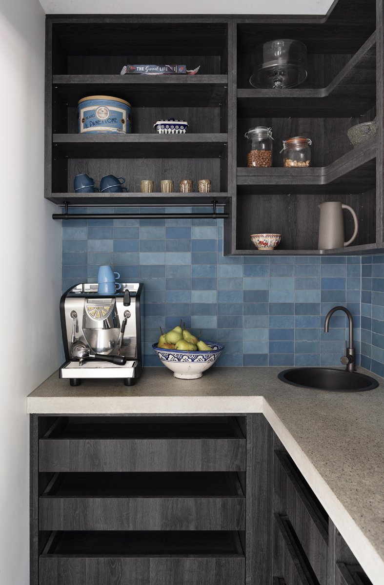 Kitchen corner with dark wood open shelves, blue tiled backsplash, a coffee machine, a bowl of green pears, a small blue cup, and a white pitcher.