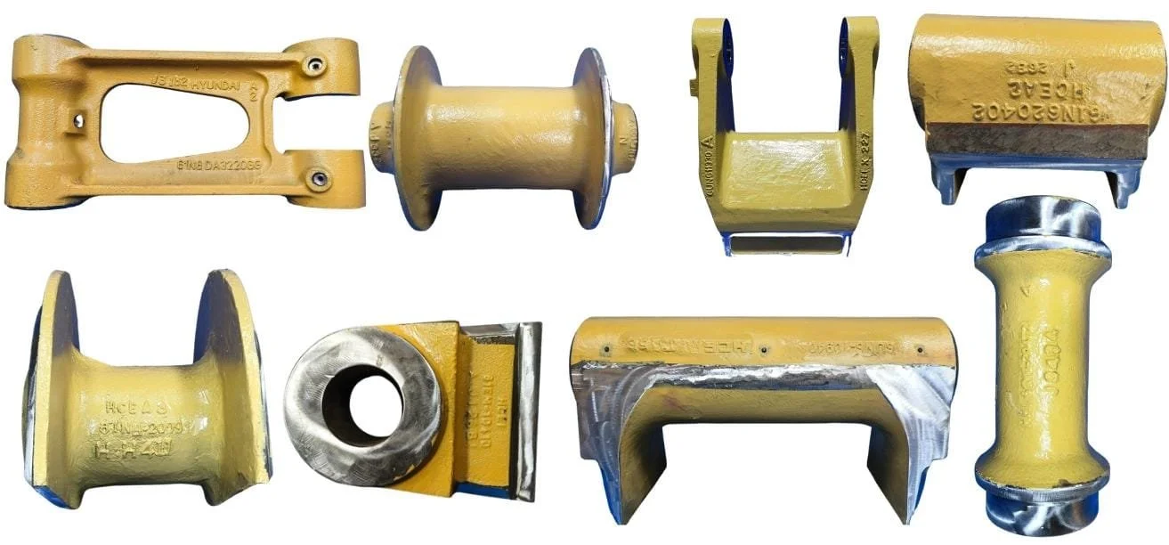 A collection of yellow and metallic industrial metal parts arranged in two rows, with various shapes including brackets, rollers, and connectors.