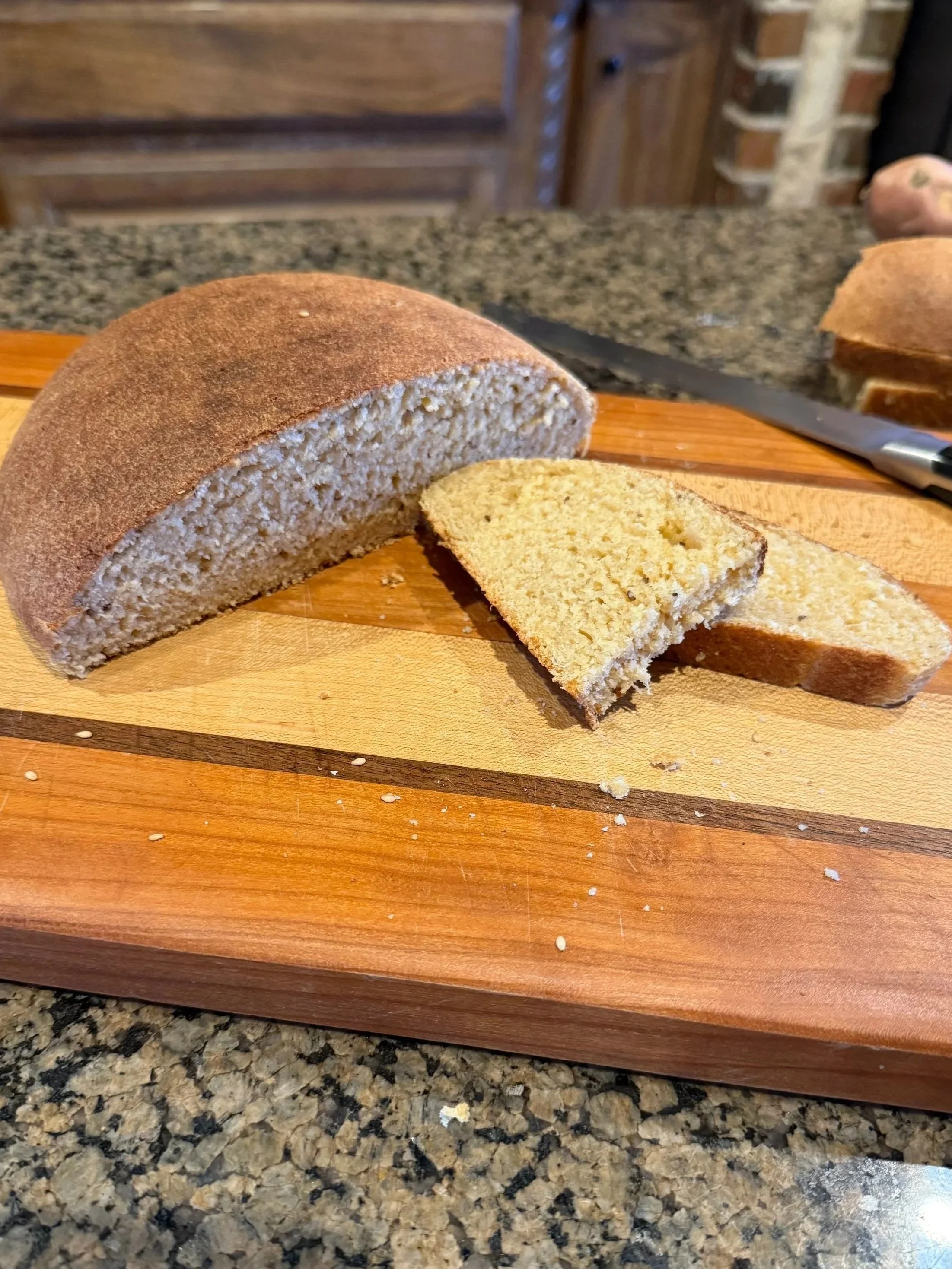 Sliced loaf of bread on a wooden cutting board on a kitchen countertop, with a piece partially cut and a knife nearby.