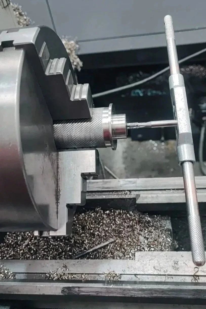 Una pieza de maquinaria de torno en proceso de fabricación con herramientas y virutas de metal alrededor.