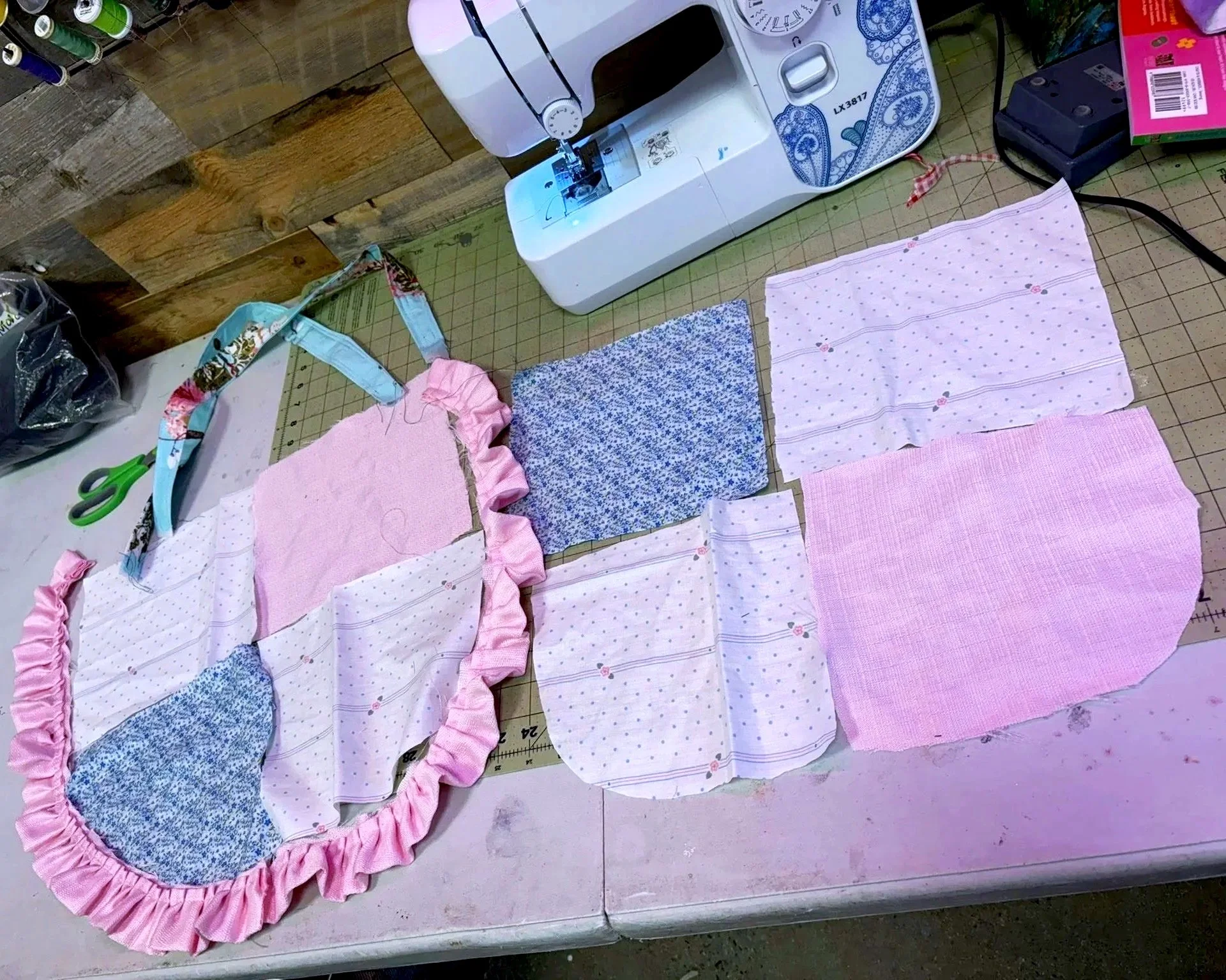 A sewing workspace with fabric pieces cut out for a project, a sewing machine, scissors, and other sewing supplies.