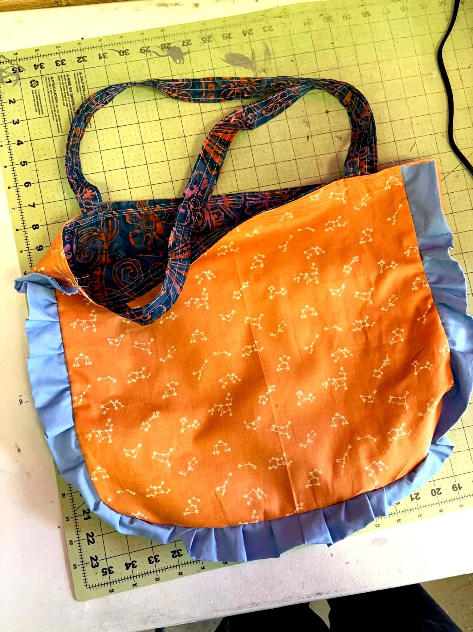 Colorful fabric tote bag with orange, blue, and patterned handles, placed on a cutting mat with measuring grid.