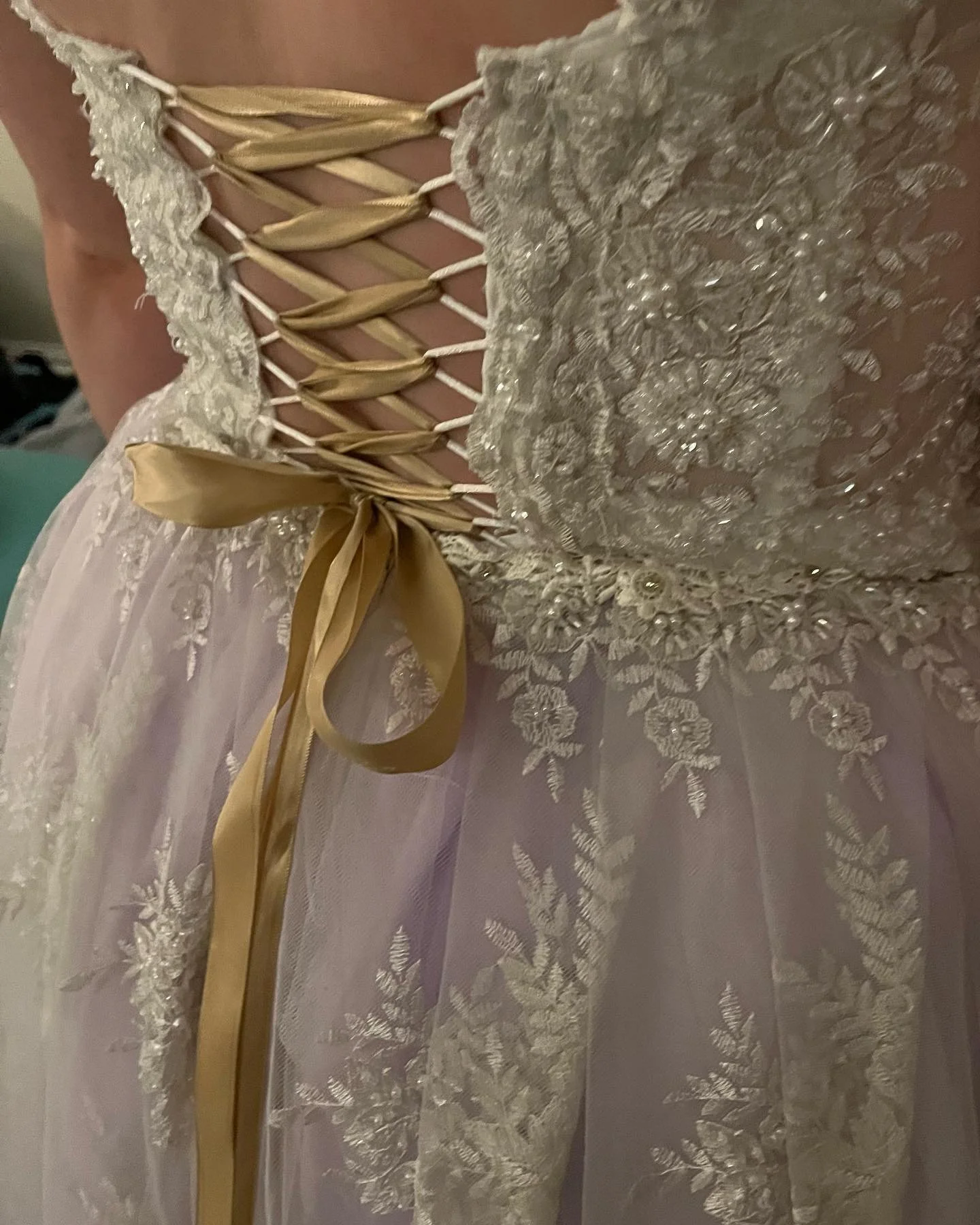 Close-up of a wedding dress with lace and floral embroidery detail, gold ribbon laced through the back, tied into a bow.