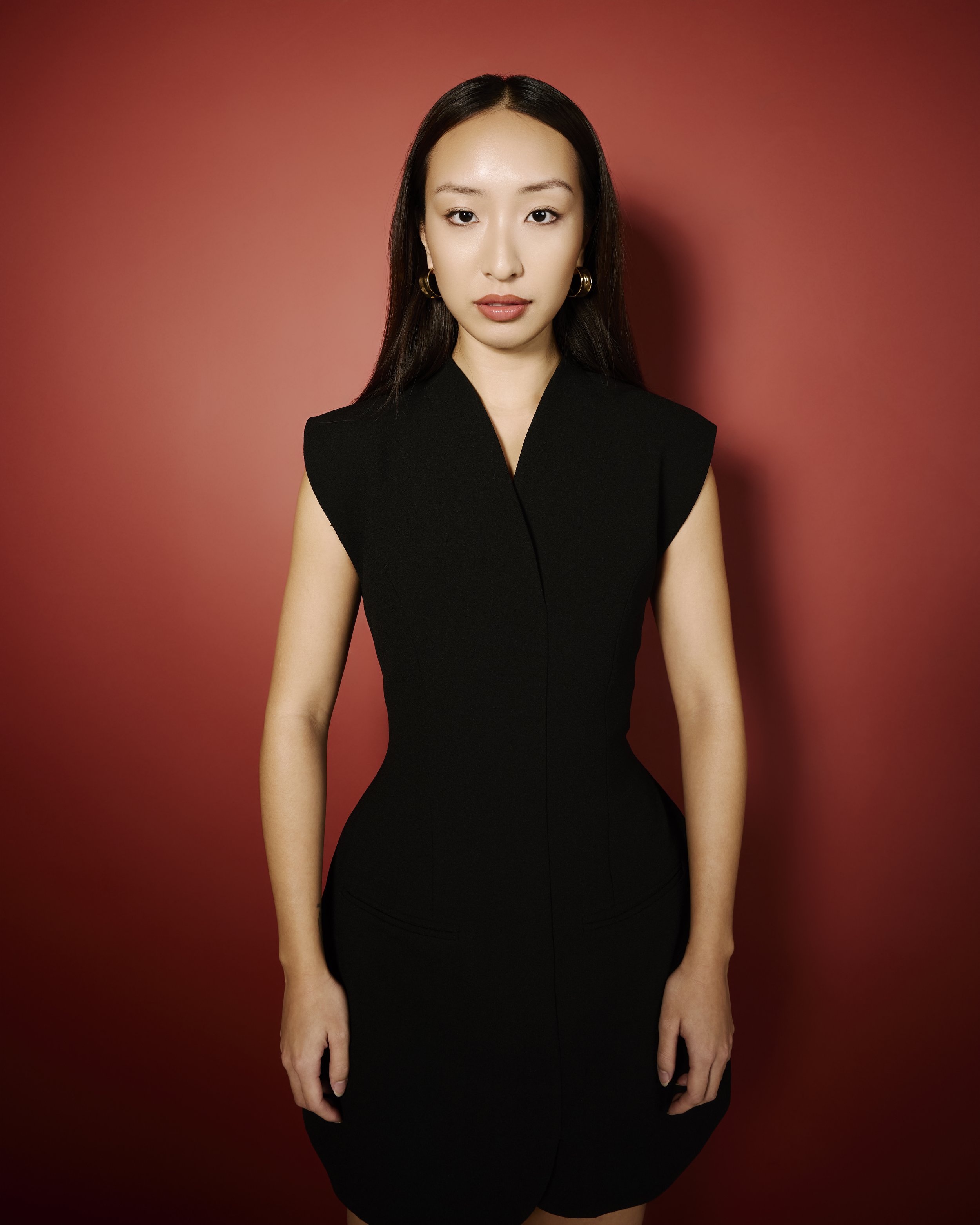 A woman in a black dress standing against a red backdrop.