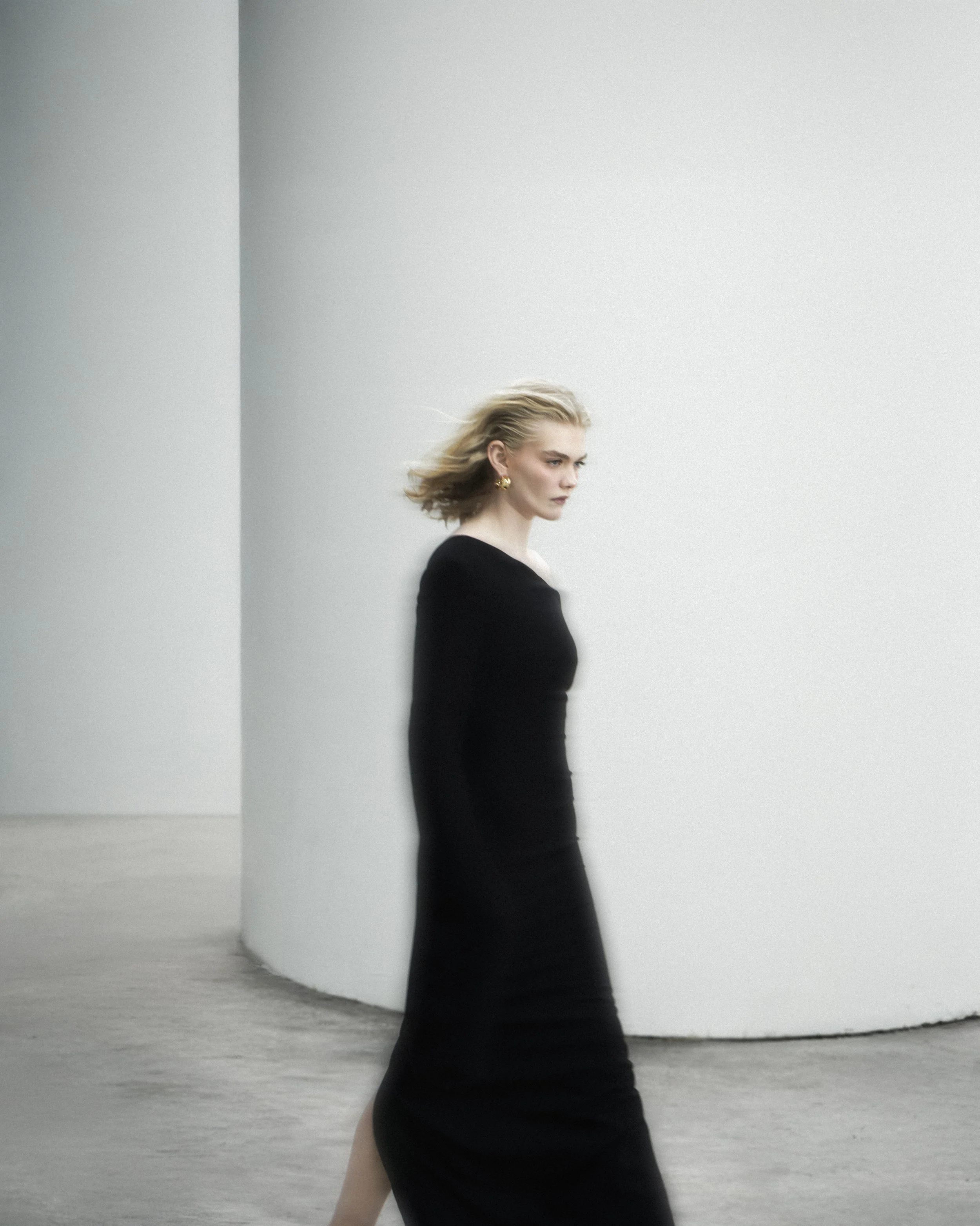 A woman in a long black dress walking past a curved white wall.
