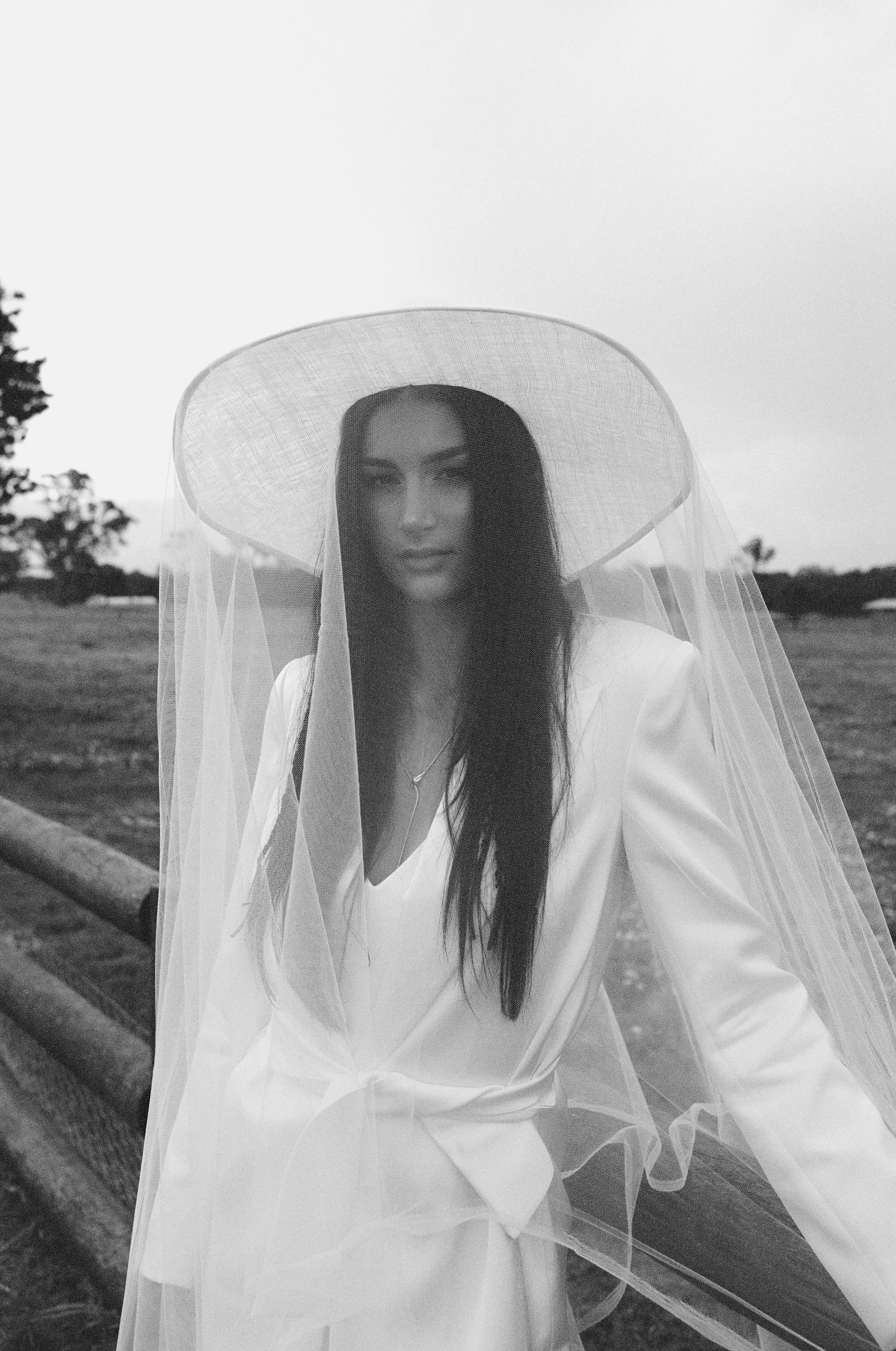 A woman wearing a large sun hat, veil, and elegant white outfit outdoors.