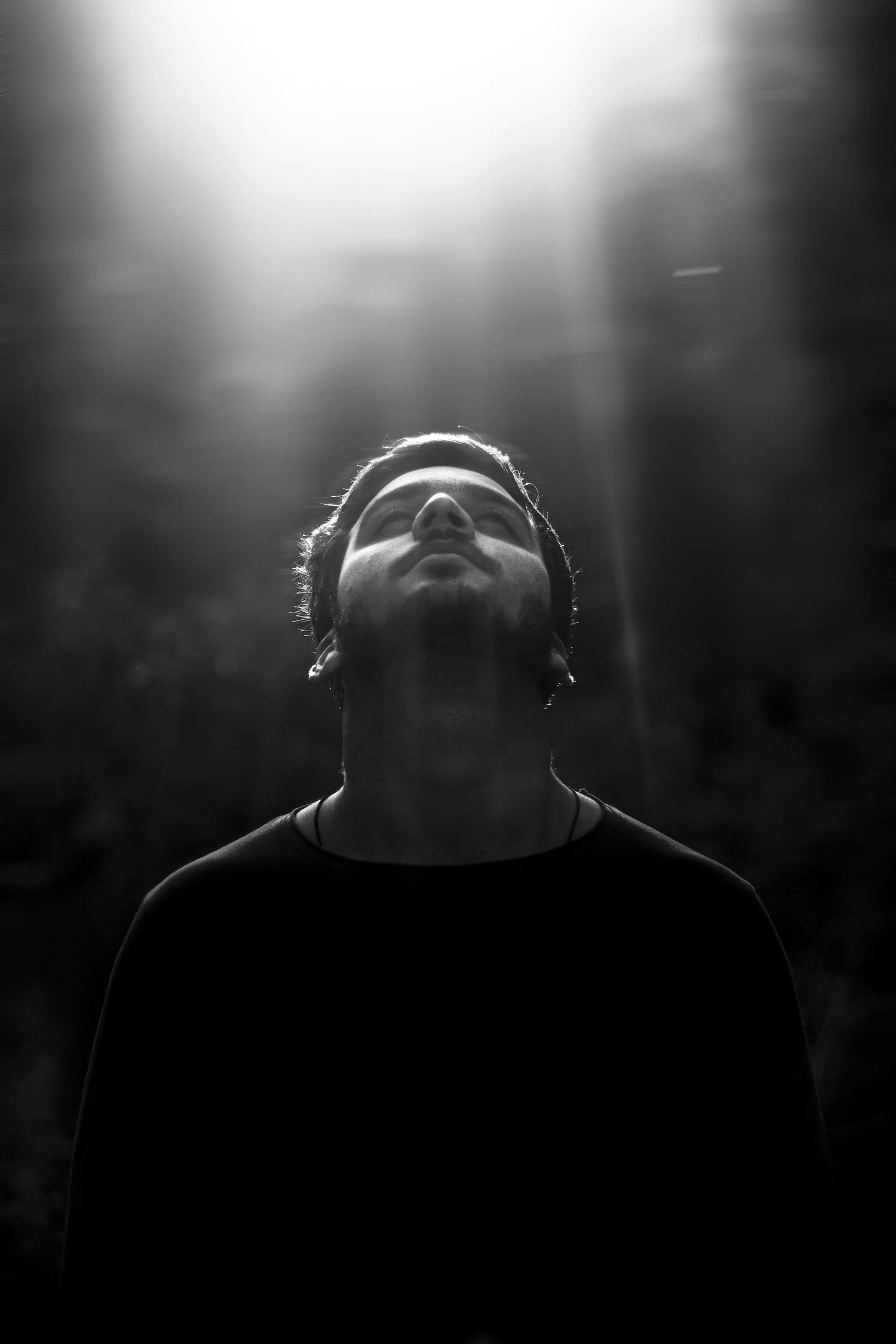 Black and white portrait of a man looking upward with a beam of light shining down.