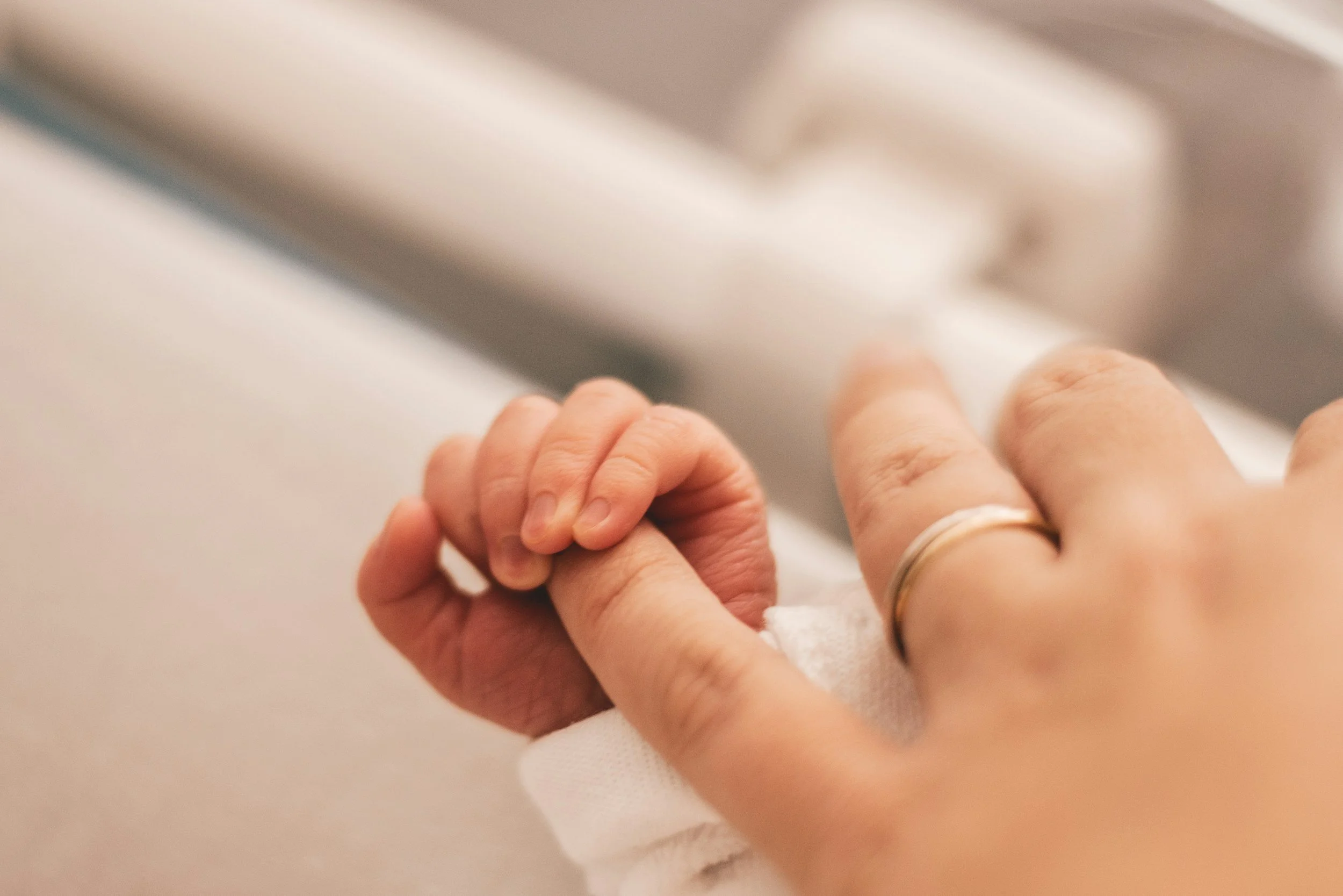 Close-up of a newborn hand wrapped around an adult finger + Mother Messenger + reassurance and emotional safety