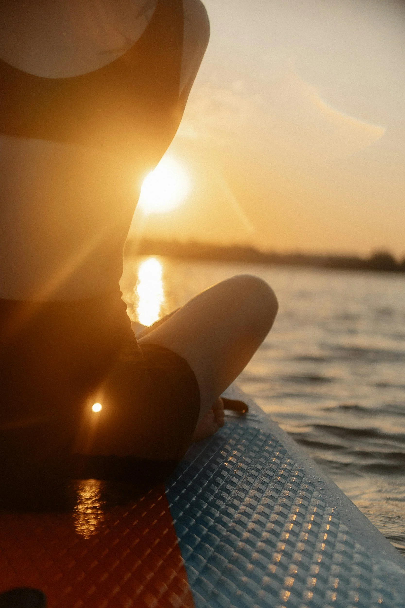Person sitting quietly on a paddleboard at sunset over calm water + Soul Messenger + reconnection to your deeper self