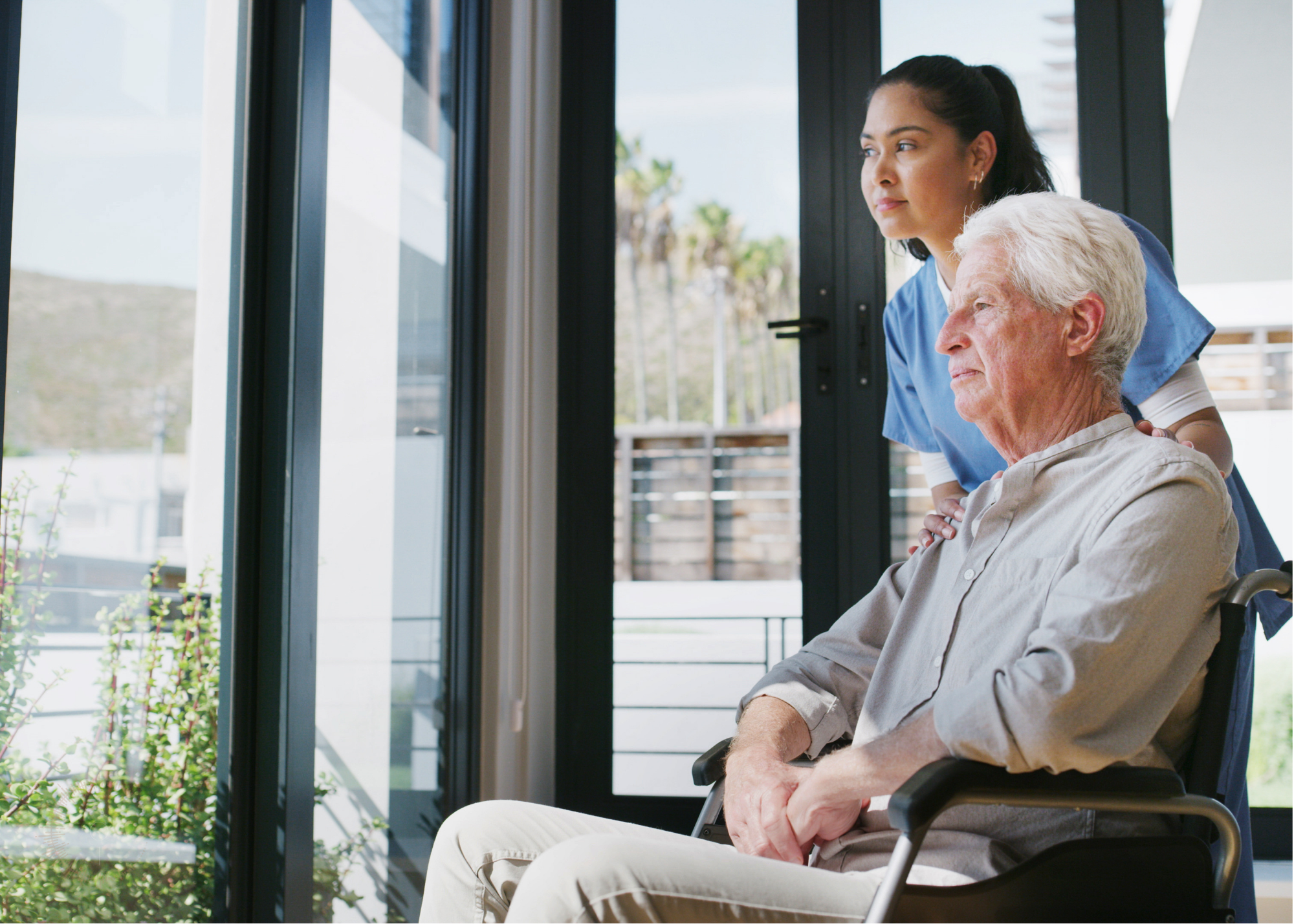 Caregiver and older adult sitting together near a window in a senior living community.