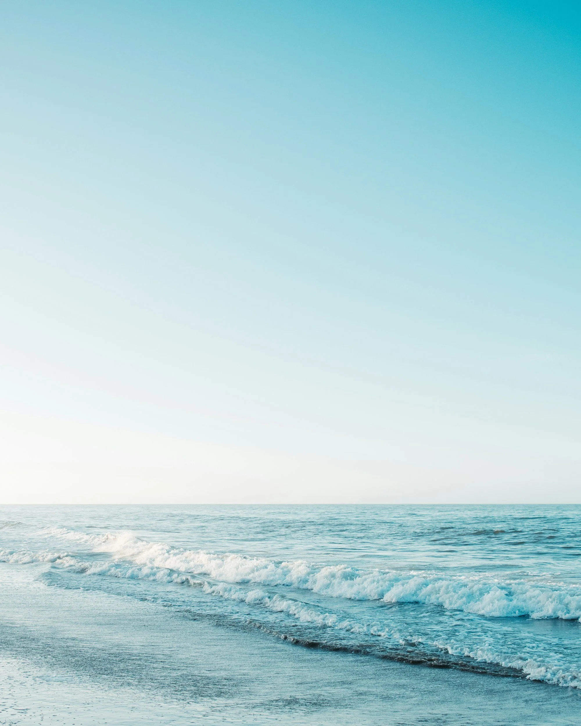 A serene beach scene with gentle waves reaching the shore and a clear, blue sky above.