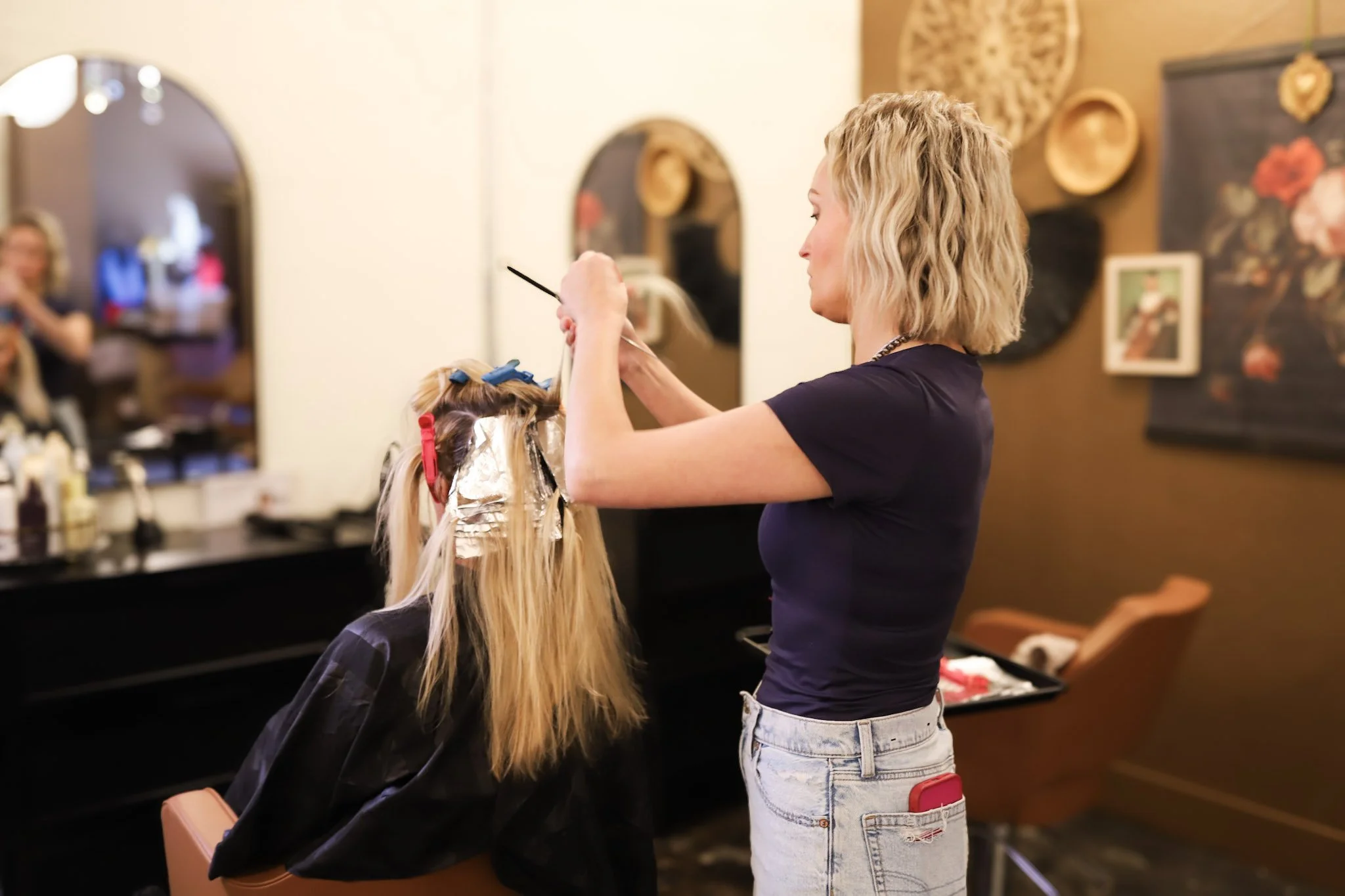 Hairdresser applying foil highlights to woman's blonde hair in salon.