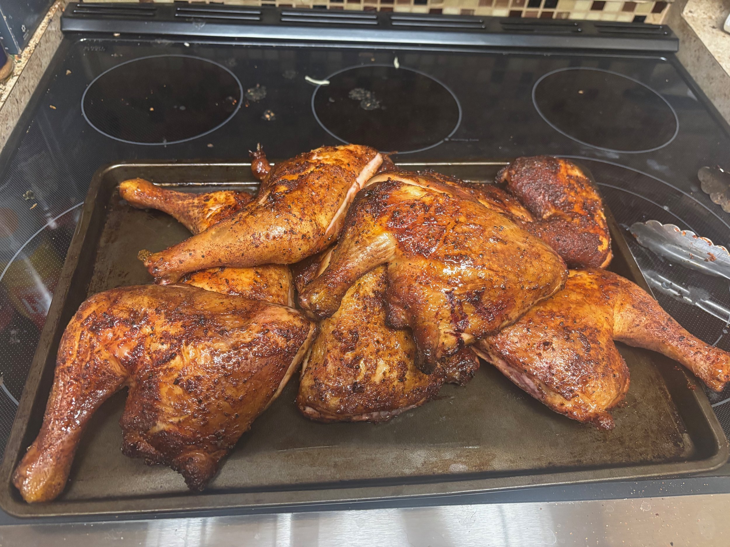 Four baked chicken halves on a roasting sheet, seasoned and cooked, resting on a stovetop.