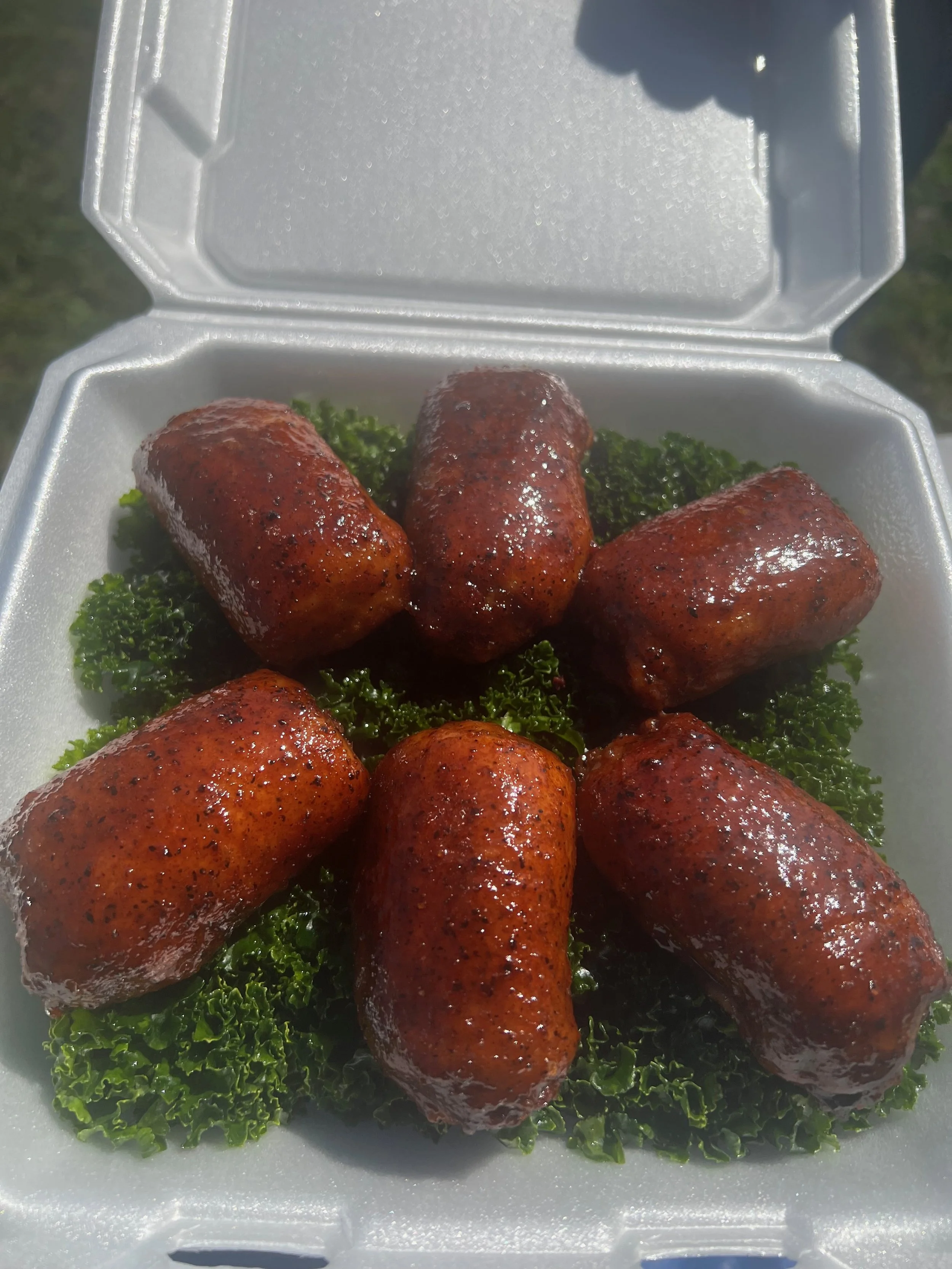 Six glazed sausages arranged on green curly parsley inside a foam takeout container.