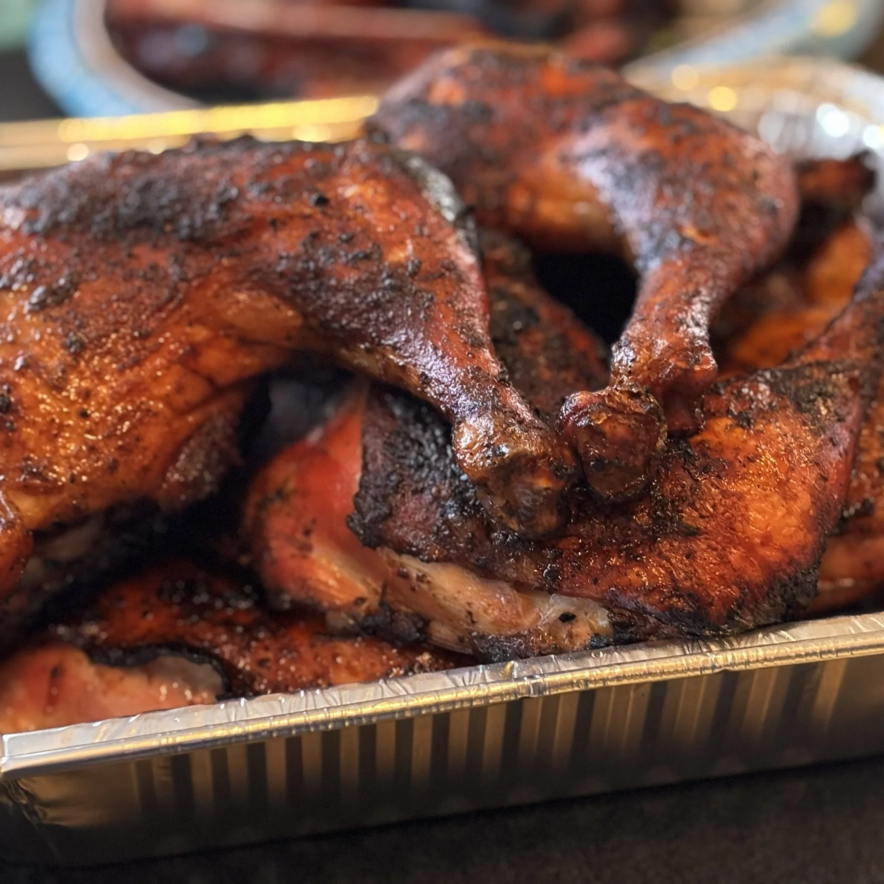 Close-up of grilled, seasoned chicken halves in a metal tray.