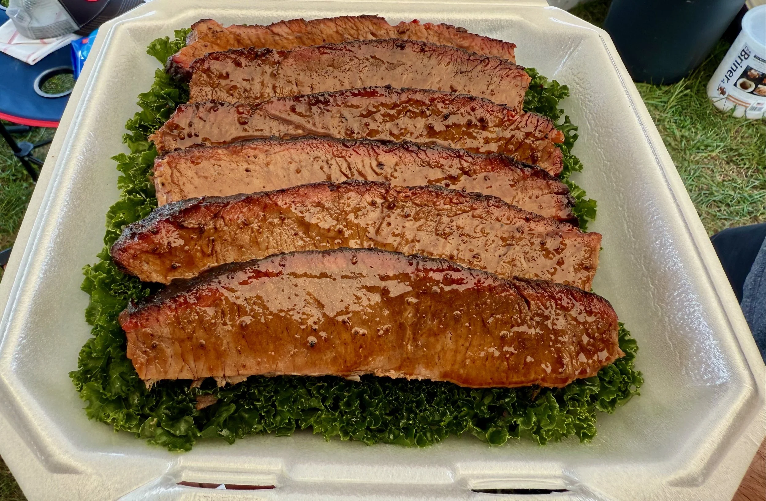 Sliced glazed salmon fillets on a bed of green curly lettuce inside a foam takeout container.