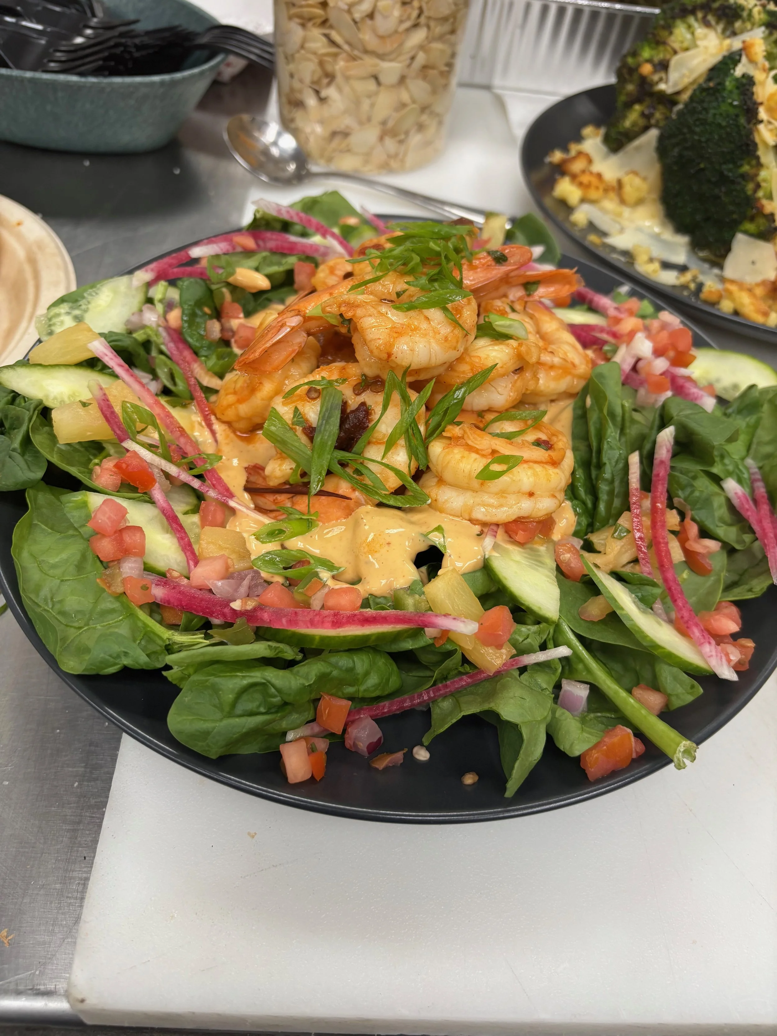 A seafood salad with shrimp on a bed of mixed greens, cucumbers, pickled onions, tomatoes, and diced vegetables, garnished with chopped green onions.
