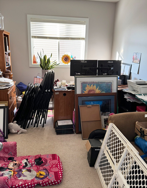 Cluttered Calgary home office before organizing, with stacked chairs, framed art, and boxes crowding the floor.