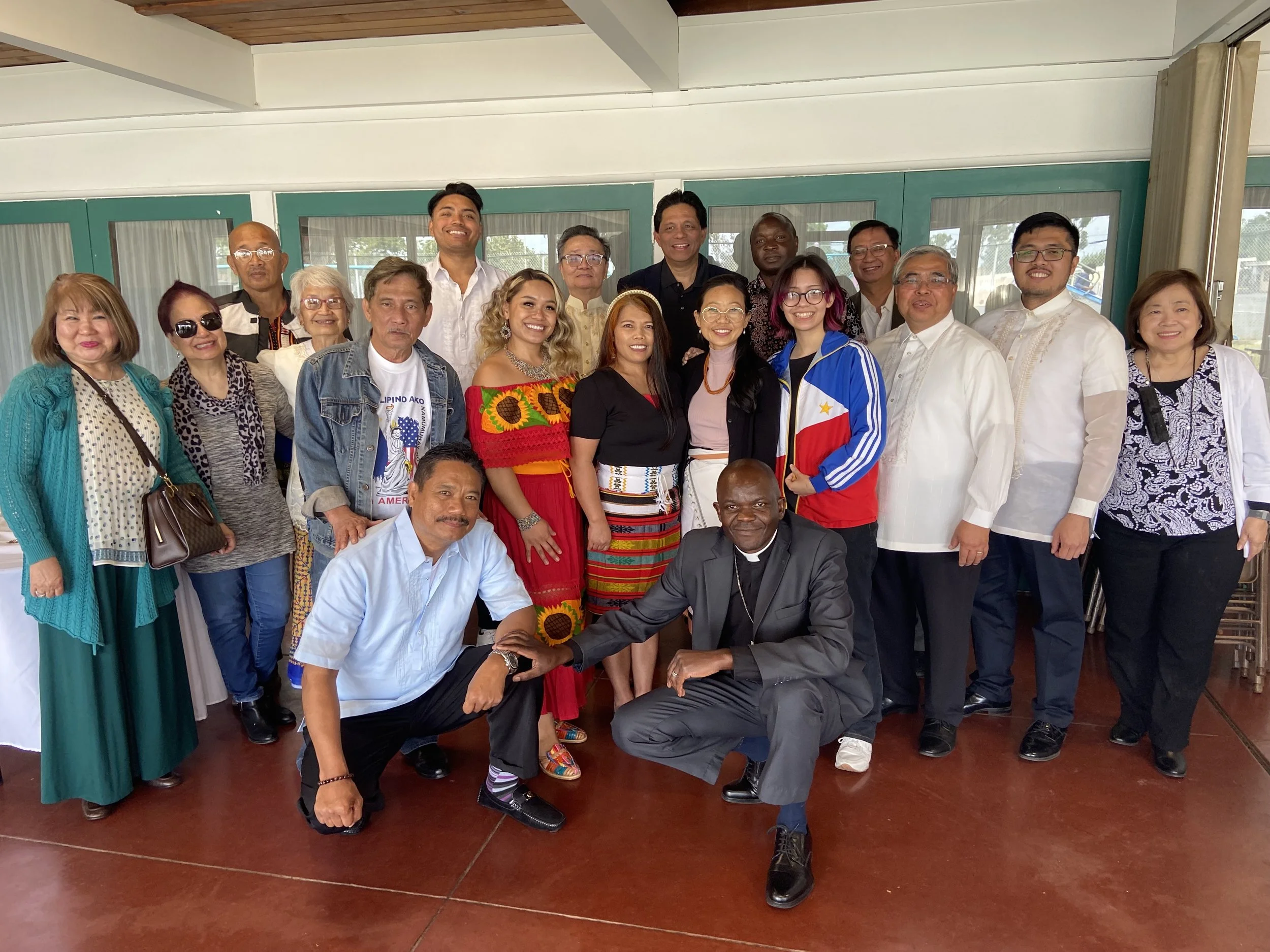 Group of diverse men and women posing together indoors for a photo, some individuals smiling and others with neutral expressions.