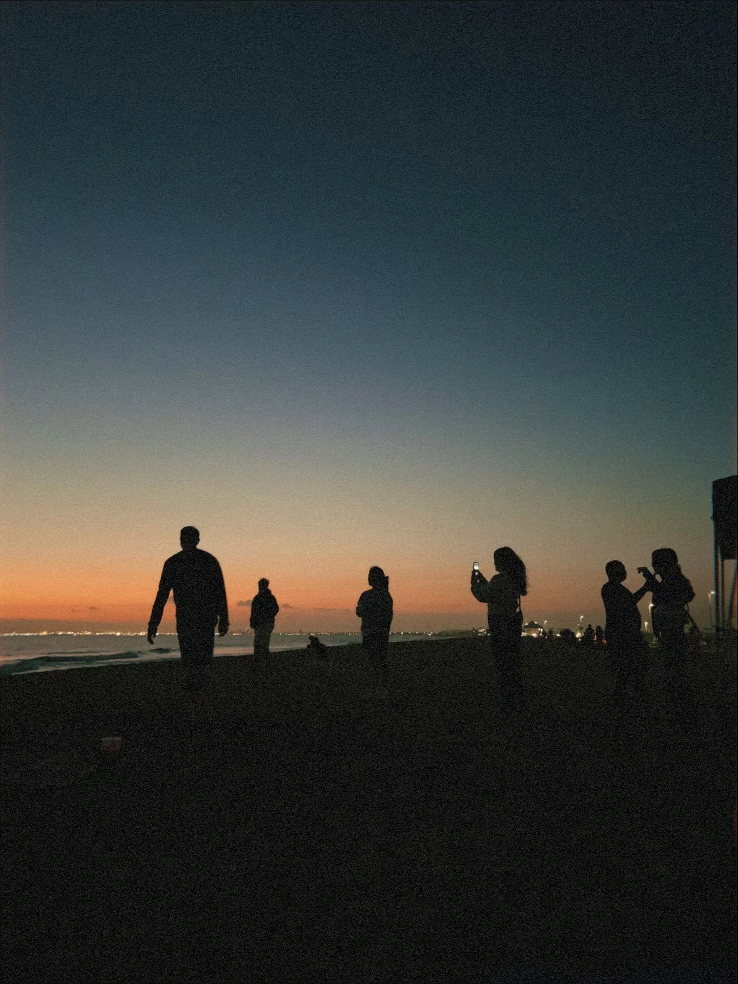 Silhouettes of people standing on a beach at sunset.
