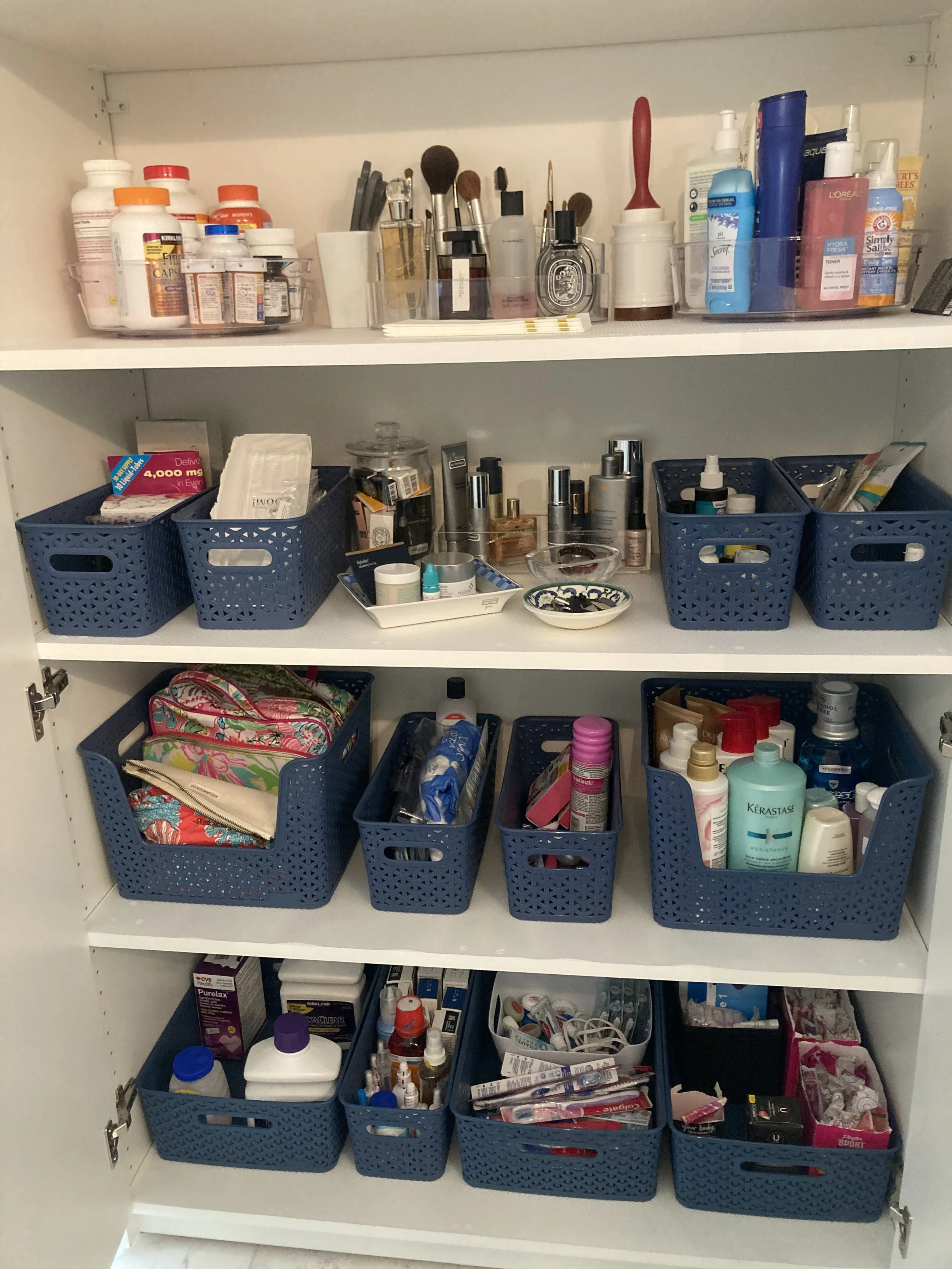 A white shelving unit filled with multiple blue baskets containing personal care items, toiletries, and makeup products.