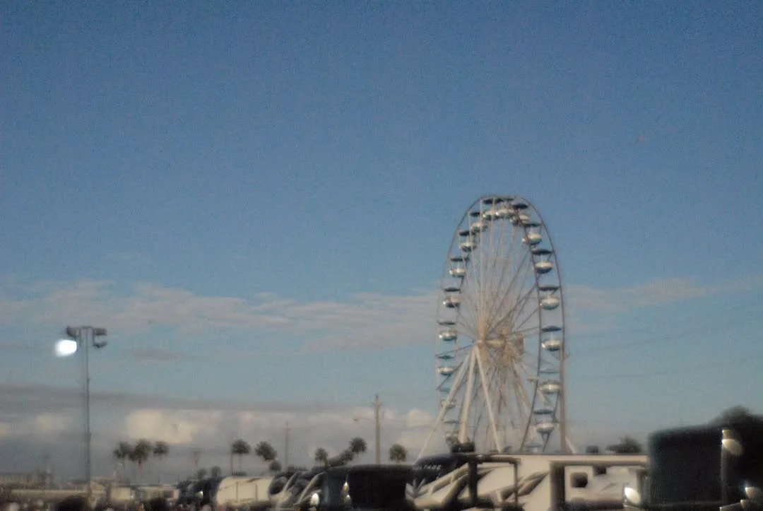 A Ferris wheel at a fairground or amusement park during daytime, with a clear blue sky in the background.