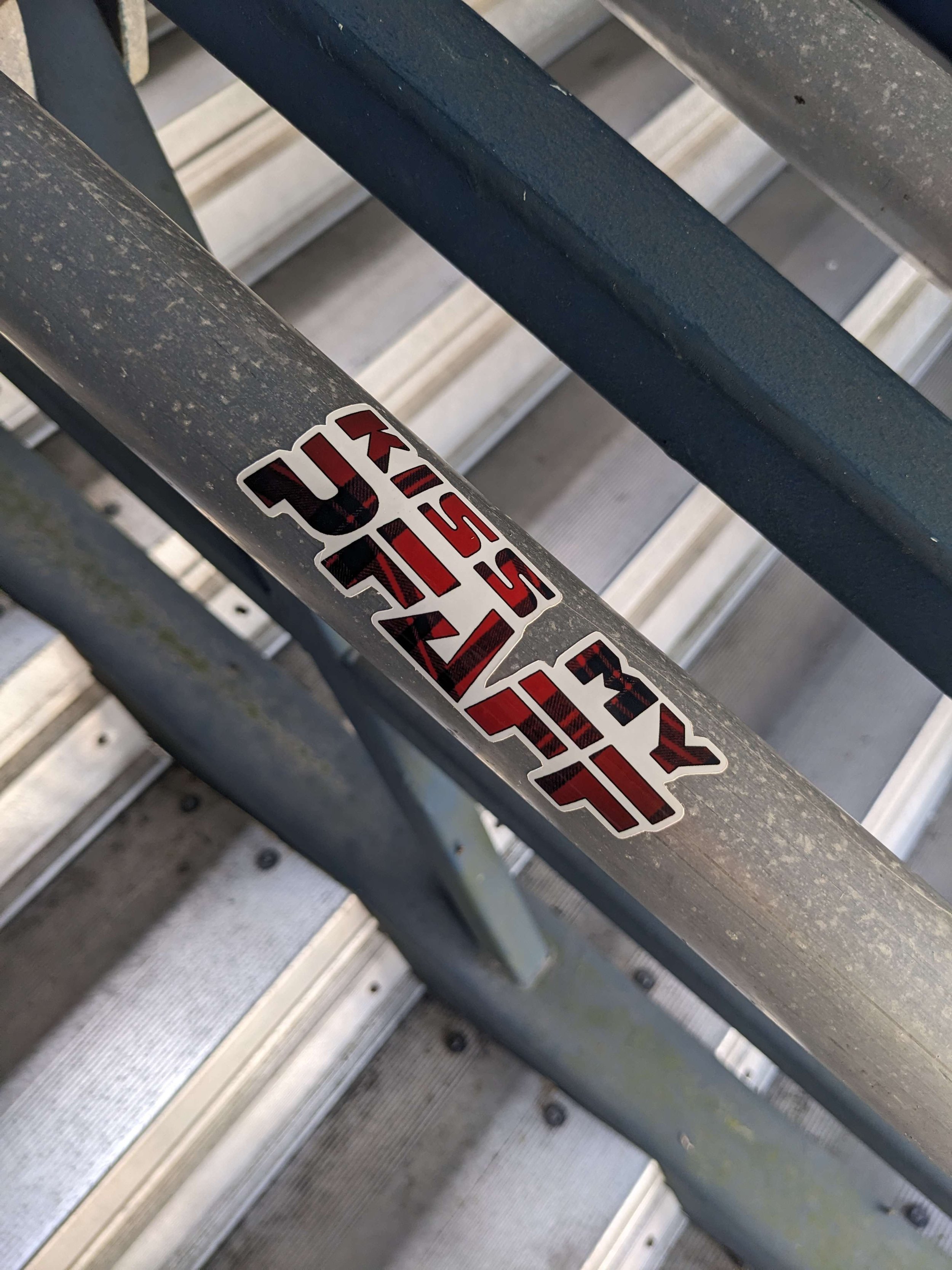 Close-up of a metal railing with a red, black, and white sticker that reads 'FALIS' in stylized text, located on a staircase with metal steps.