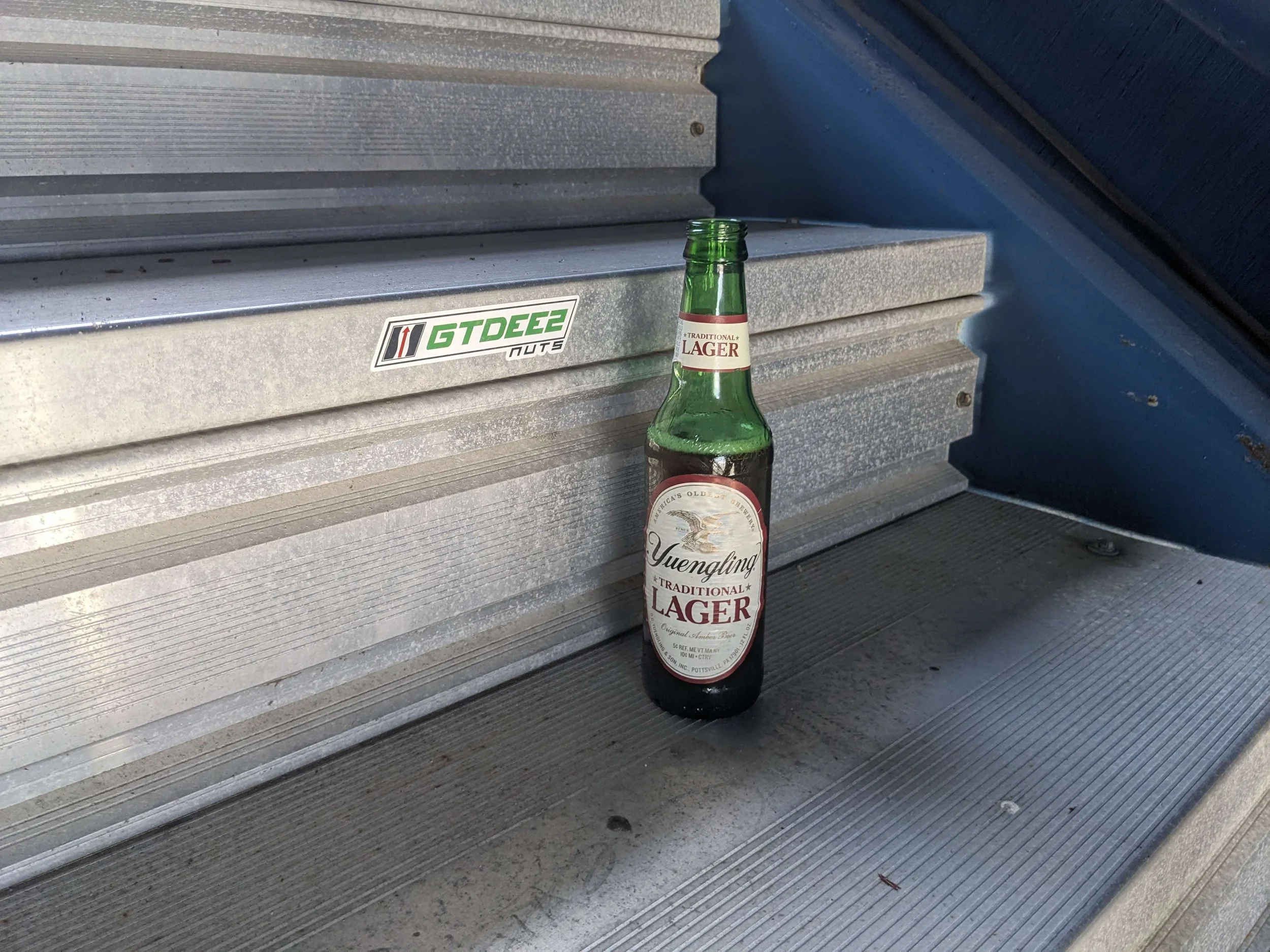A green glass bottle of Yuengling Traditional Lager beer placed on a metal stair step.