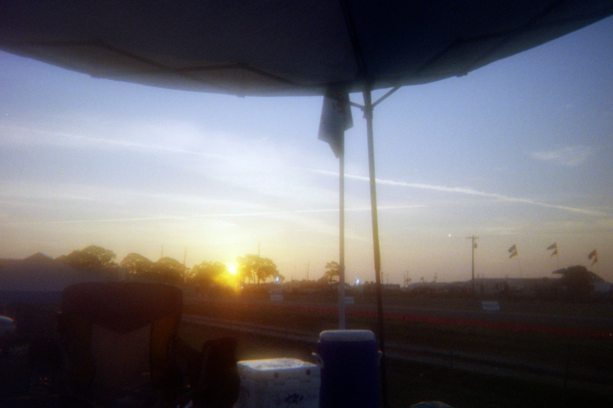 Sunset over a racetrack with flags, trees, and equipment in the foreground.