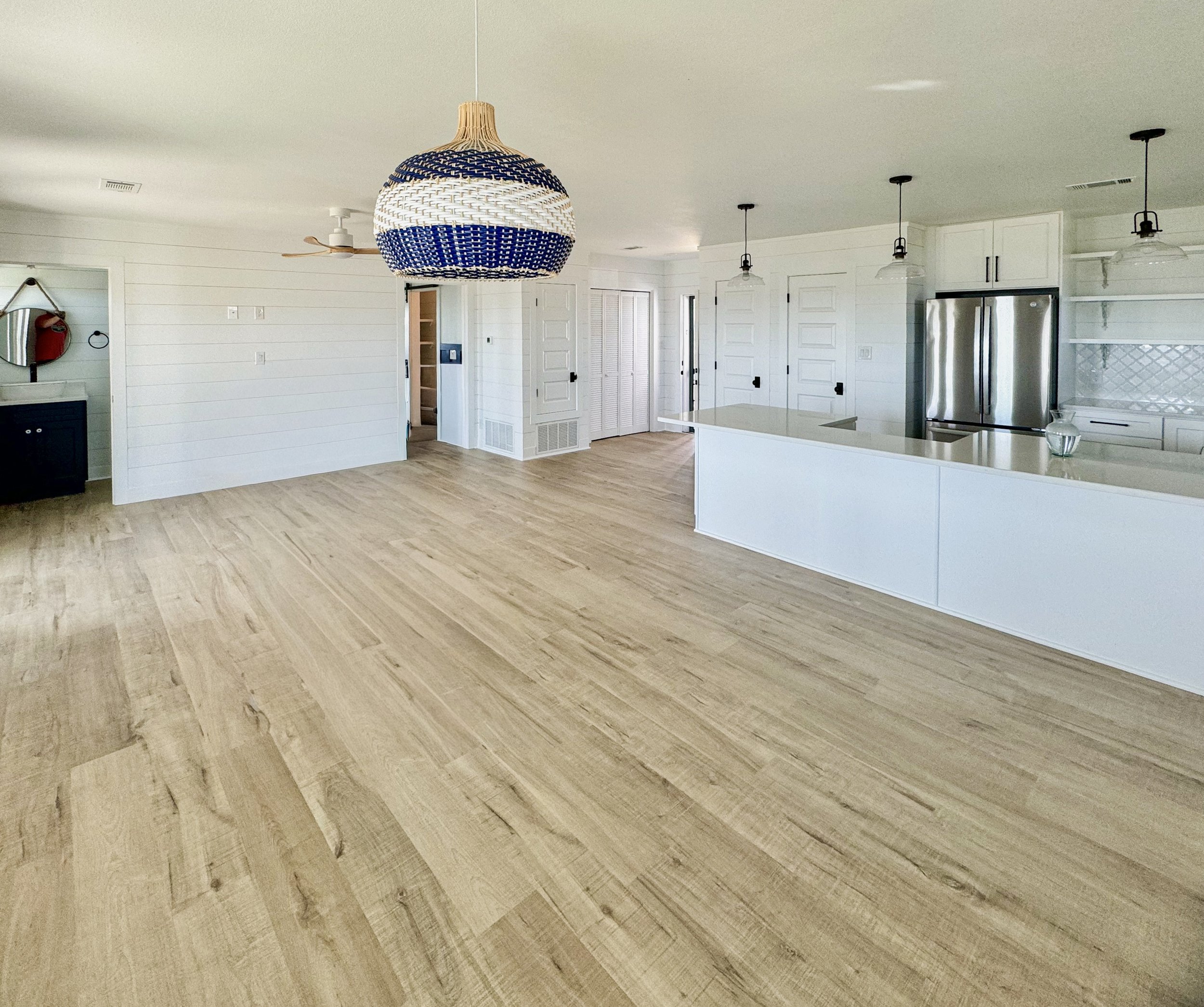 Empty open-concept kitchen and living area with white shiplap walls, wooden floors, and modern lighting fixtures.