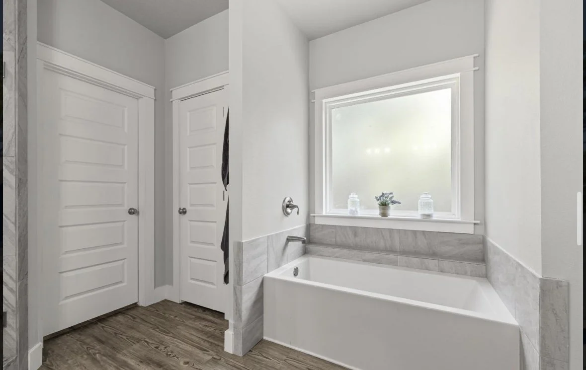 A bathroom with a bathtub, a window above it, and two closed closet doors.