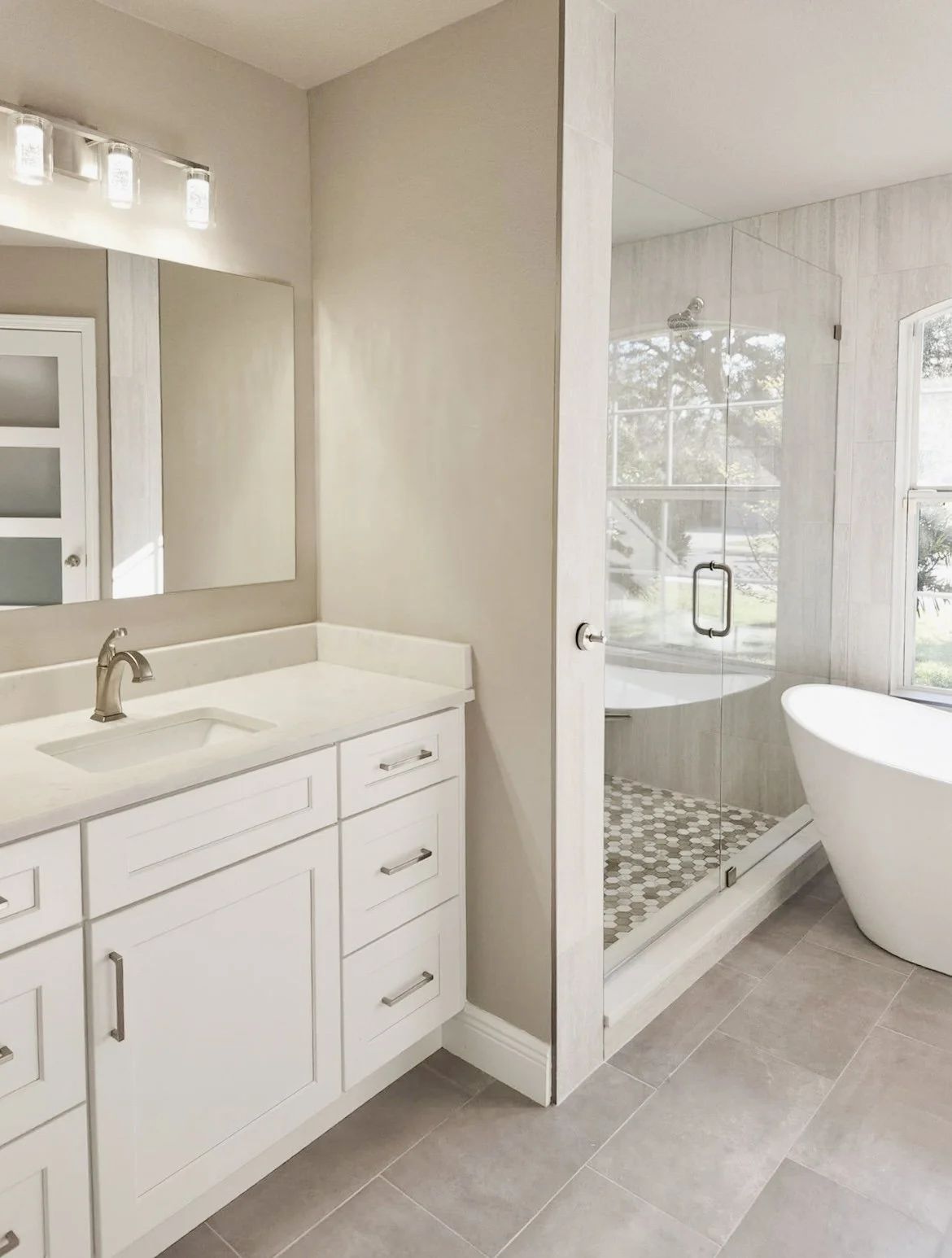 Modern bathroom with white vanity, large mirror, and a glass-enclosed shower with a bathtub nearby, natural light coming through a window.