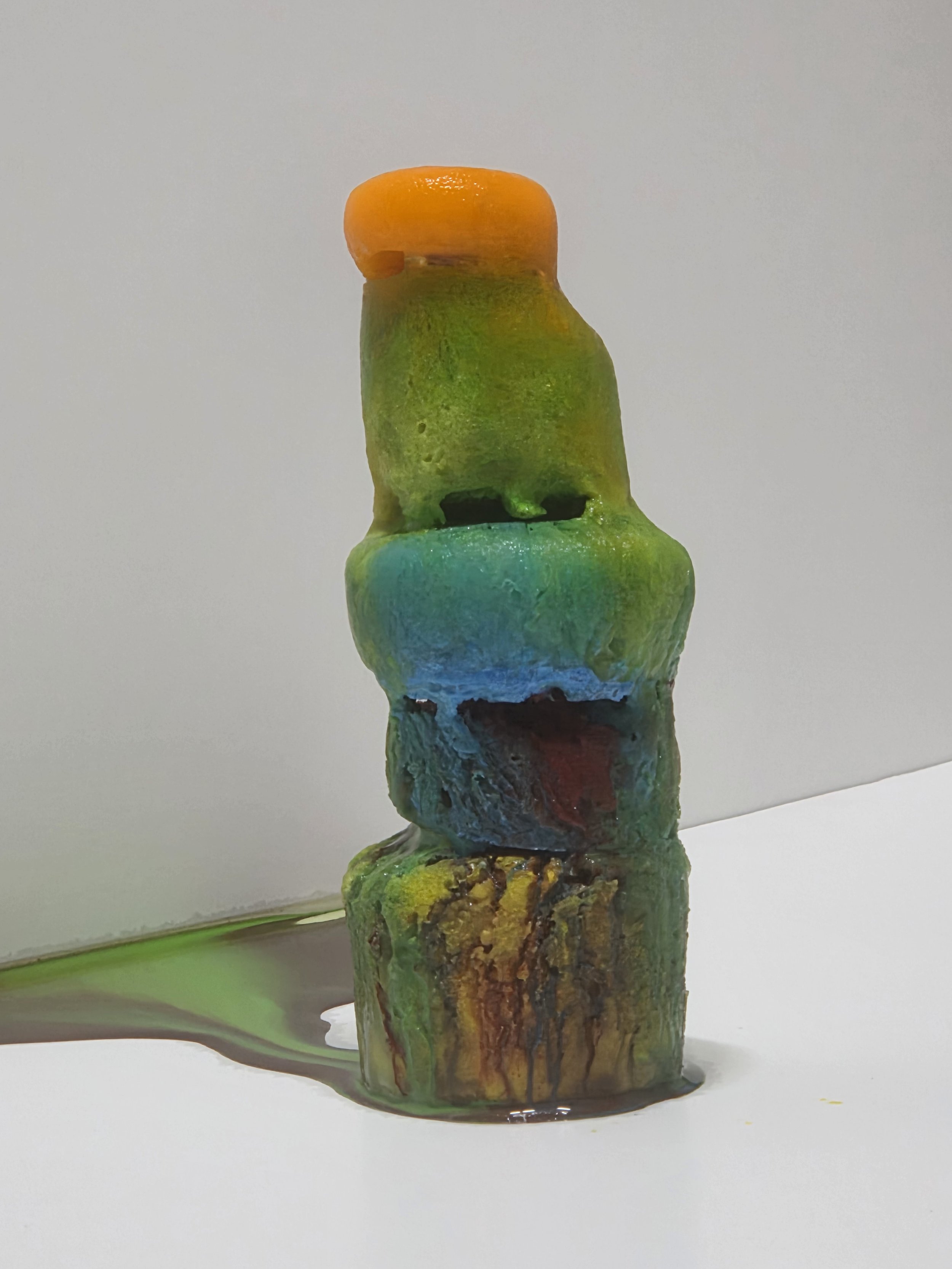Colorful abstract sculpture with multiple stacked shapes in orange, green, blue, and brown, some with textured surfaces.