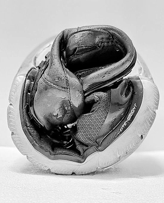 A pair of black running shoes with water drops, placed on top of a white ball.