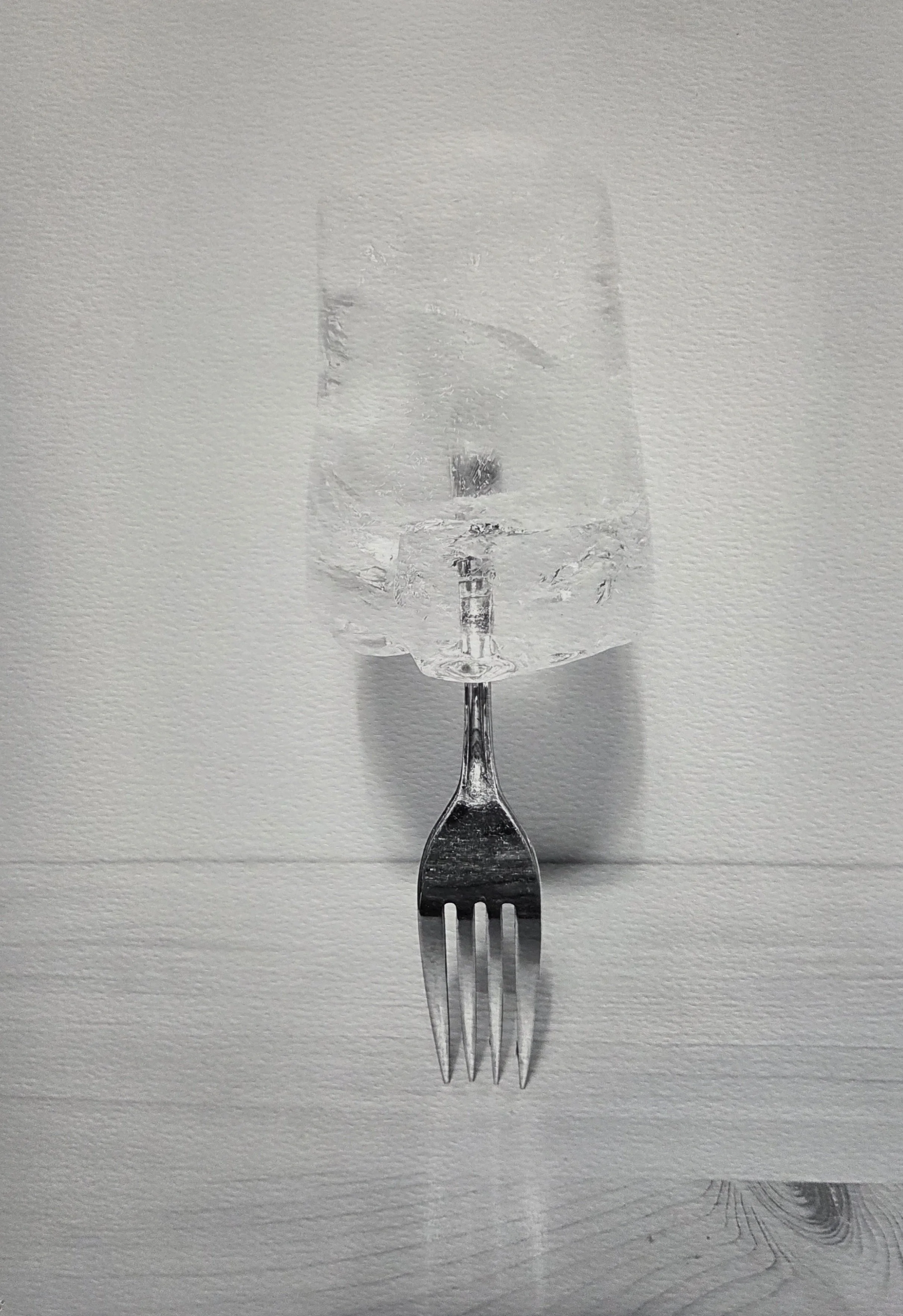 A metal fork with a glass of water on top, creating the illusion of a single object, against a plain white background.