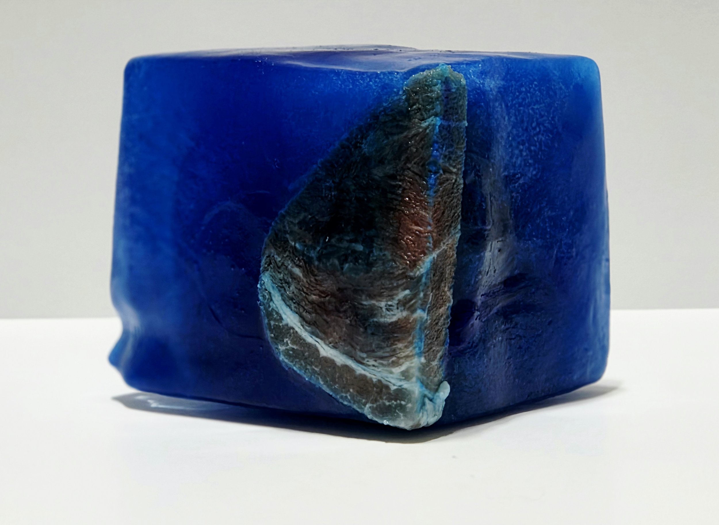 A close-up of a blue cube with a textured, irregularly shaped, multicolored piece embedded in one side.