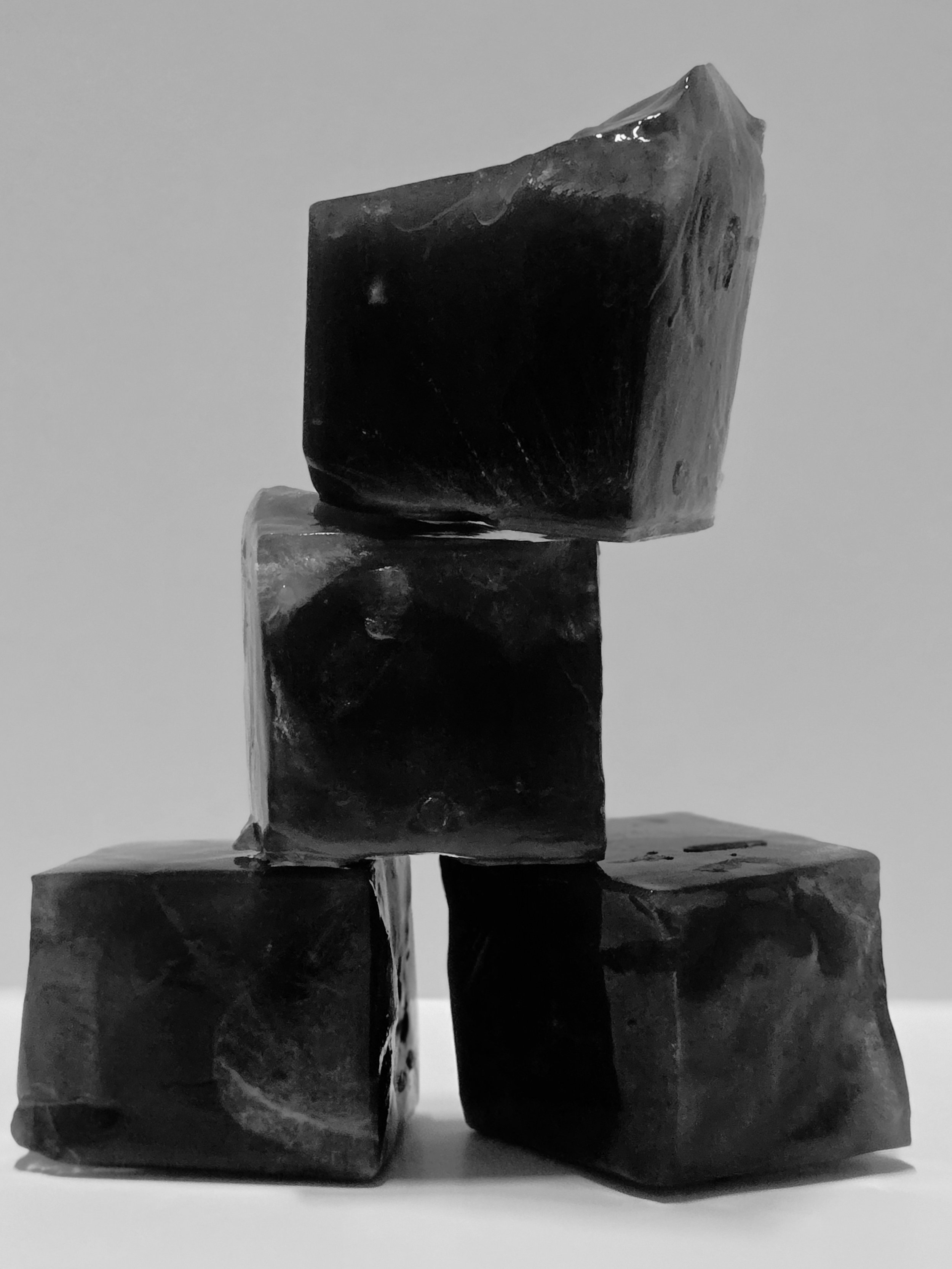 Four black irregularly shaped stones stacked in a sculpture with one stone balanced on top of three stones at the bottom, monochrome photo.