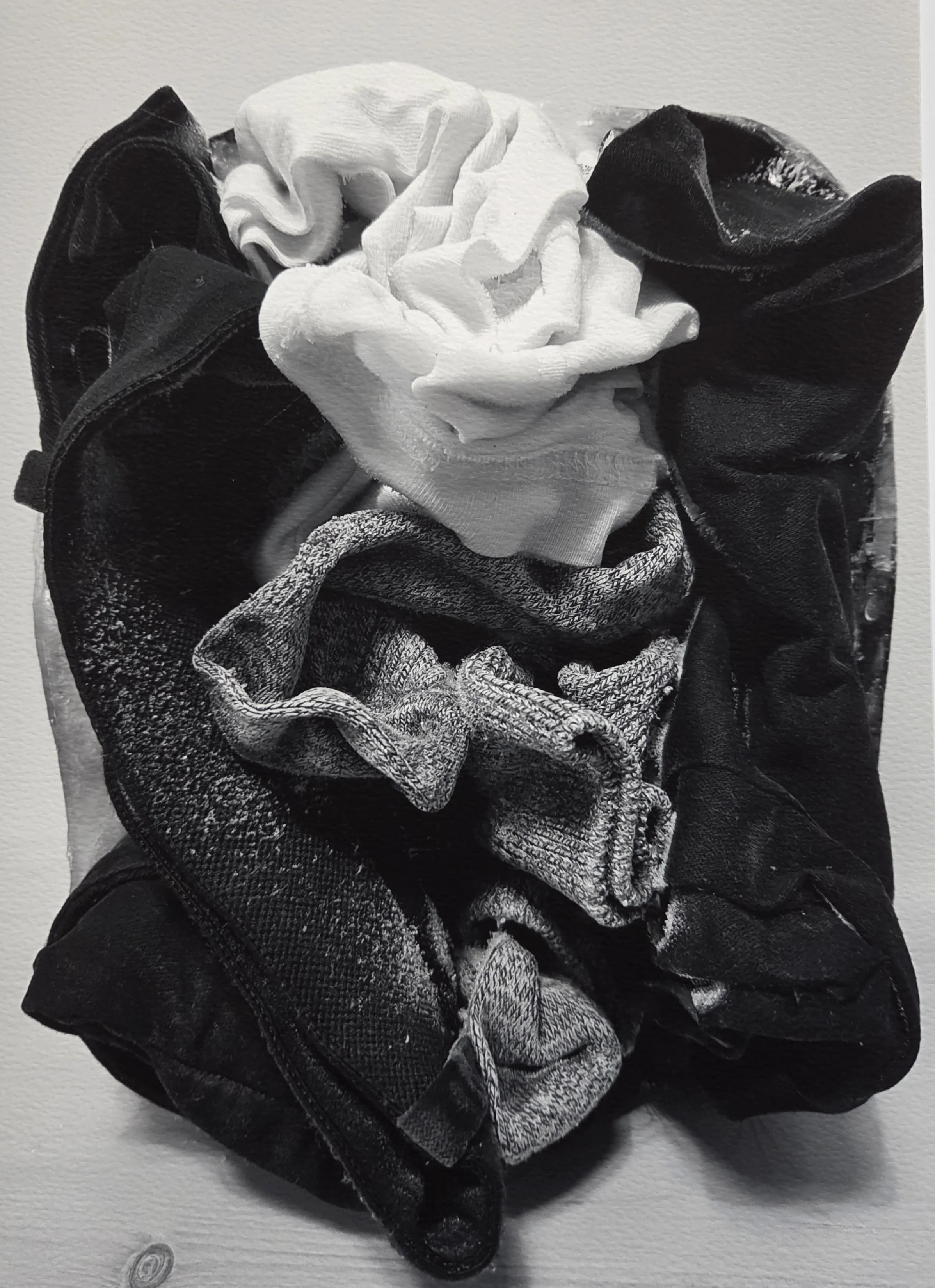 A pile of folded clothes including a white shirt, a pair of jeans, and darker-colored garments.