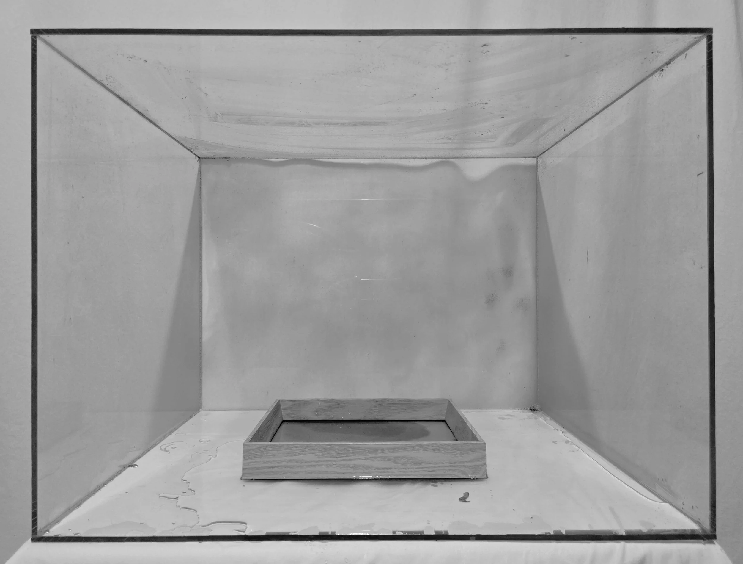 Empty metal box with sides, bottom, and a small rectangular wooden frame inside on top of a white surface.