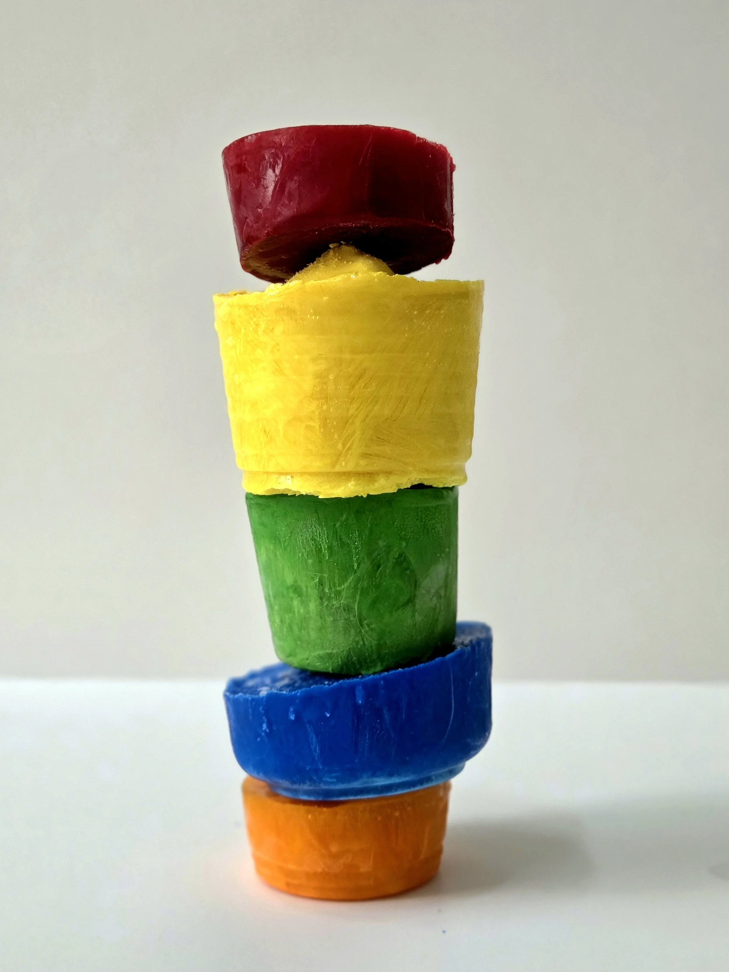 Stack of colorful, chunky fruit slices arranged vertically on a plain white surface.