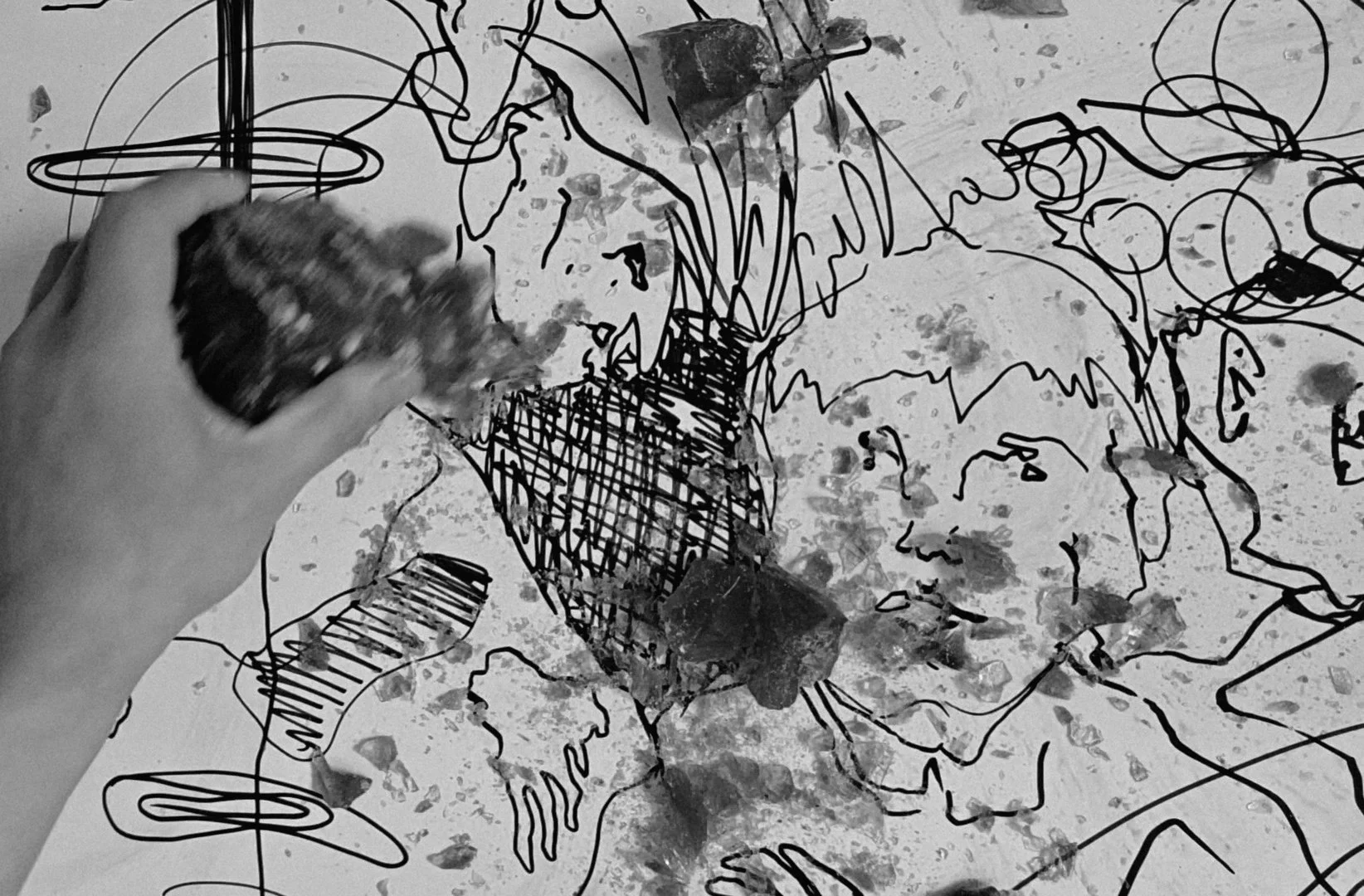 A person holding an eraser and drawing on paper with black ink. The artwork includes abstract lines, sketches of faces, and splattered ink.