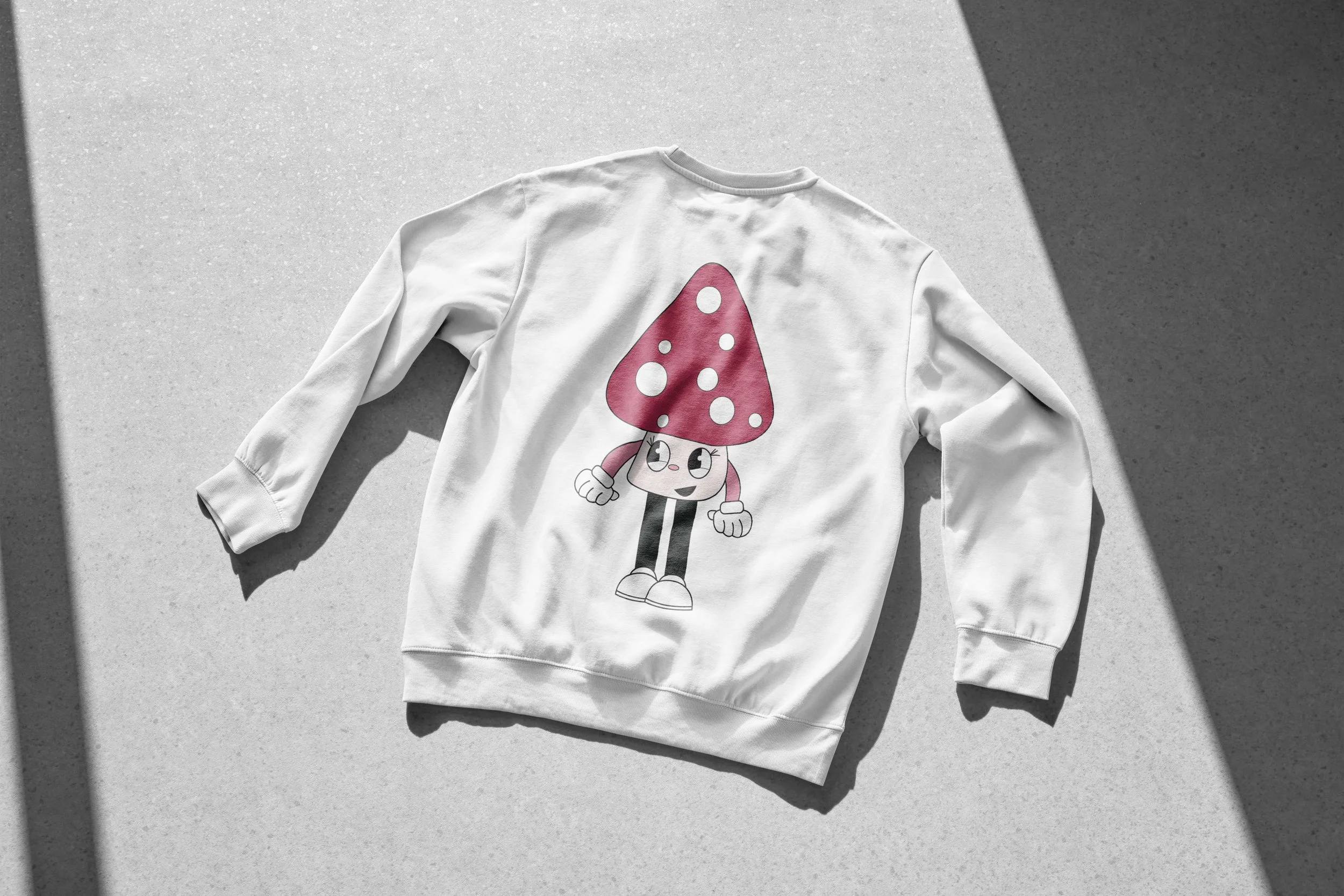 White sweatshirt laid flat, featuring a cartoon mushroom character with a red spotted cap, expressive face, gloved hands, and white shoes.