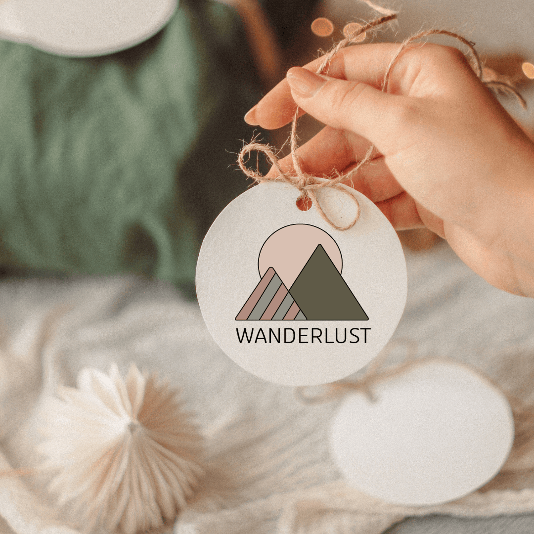 Hand holding a round paper tag with a mountain graphic and the word ‘WANDERLUST.'