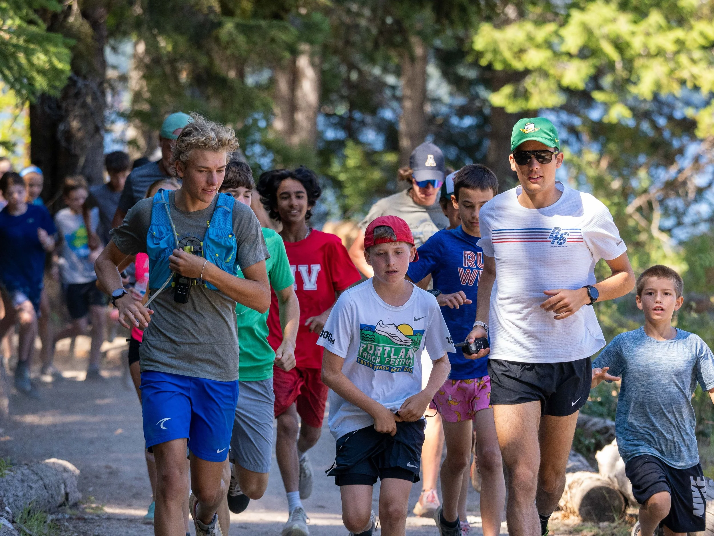 Group of athletes and teenagers participating in an outdoor trail run in a wooded area, at the Elite Middle School Camp at Youth Runner Camps