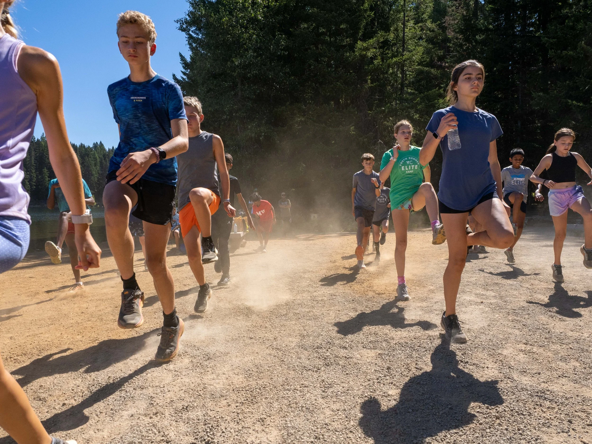 Group of children running and jumping on dirt path outdoors near a lake at the Elite Middle School Camp at Youth Runner Camps