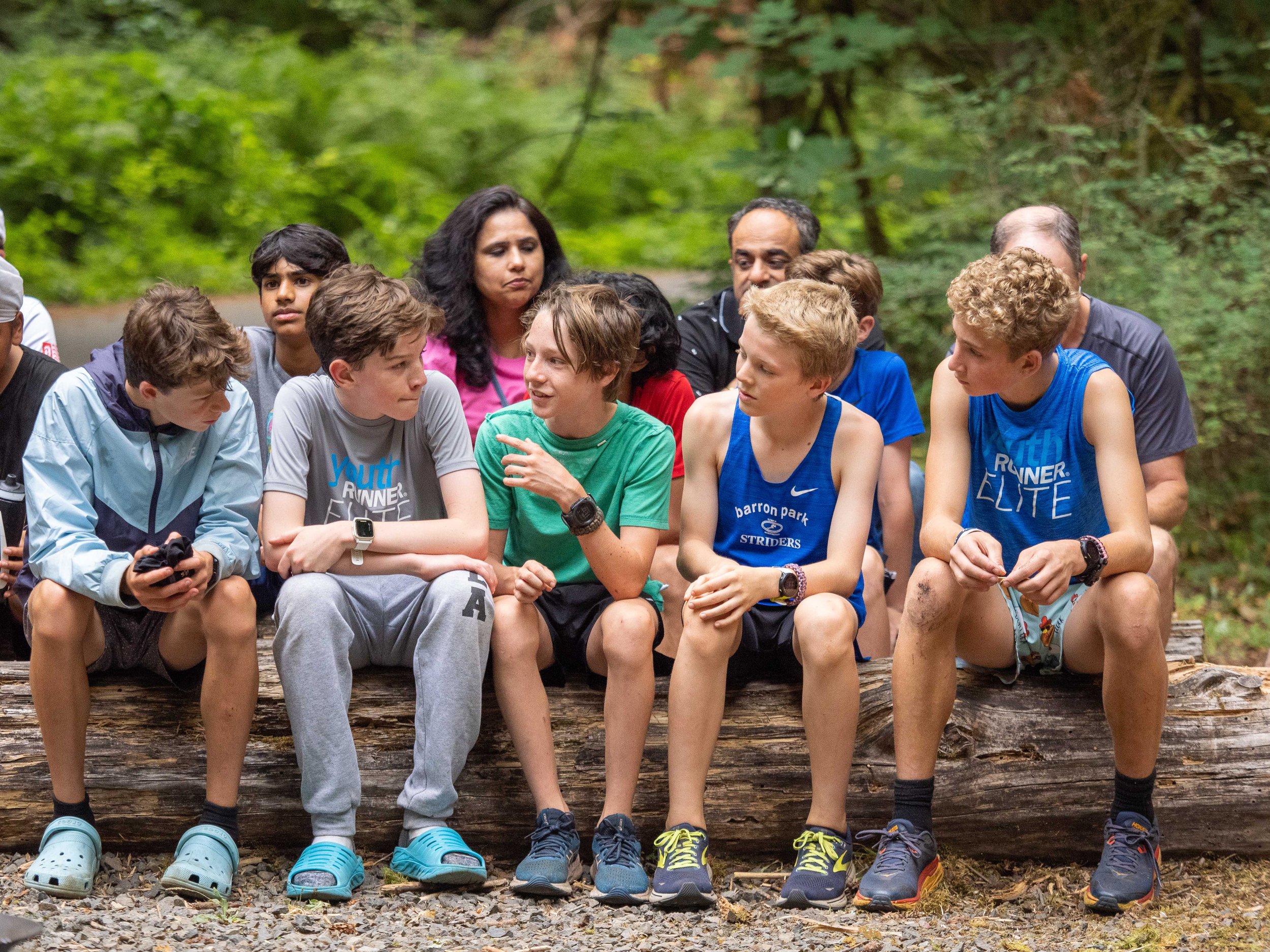 Group of young boys and adults sitting on a log during an outdoor event in a forest at the Elite Middle School Camp at Youth Runner Camps