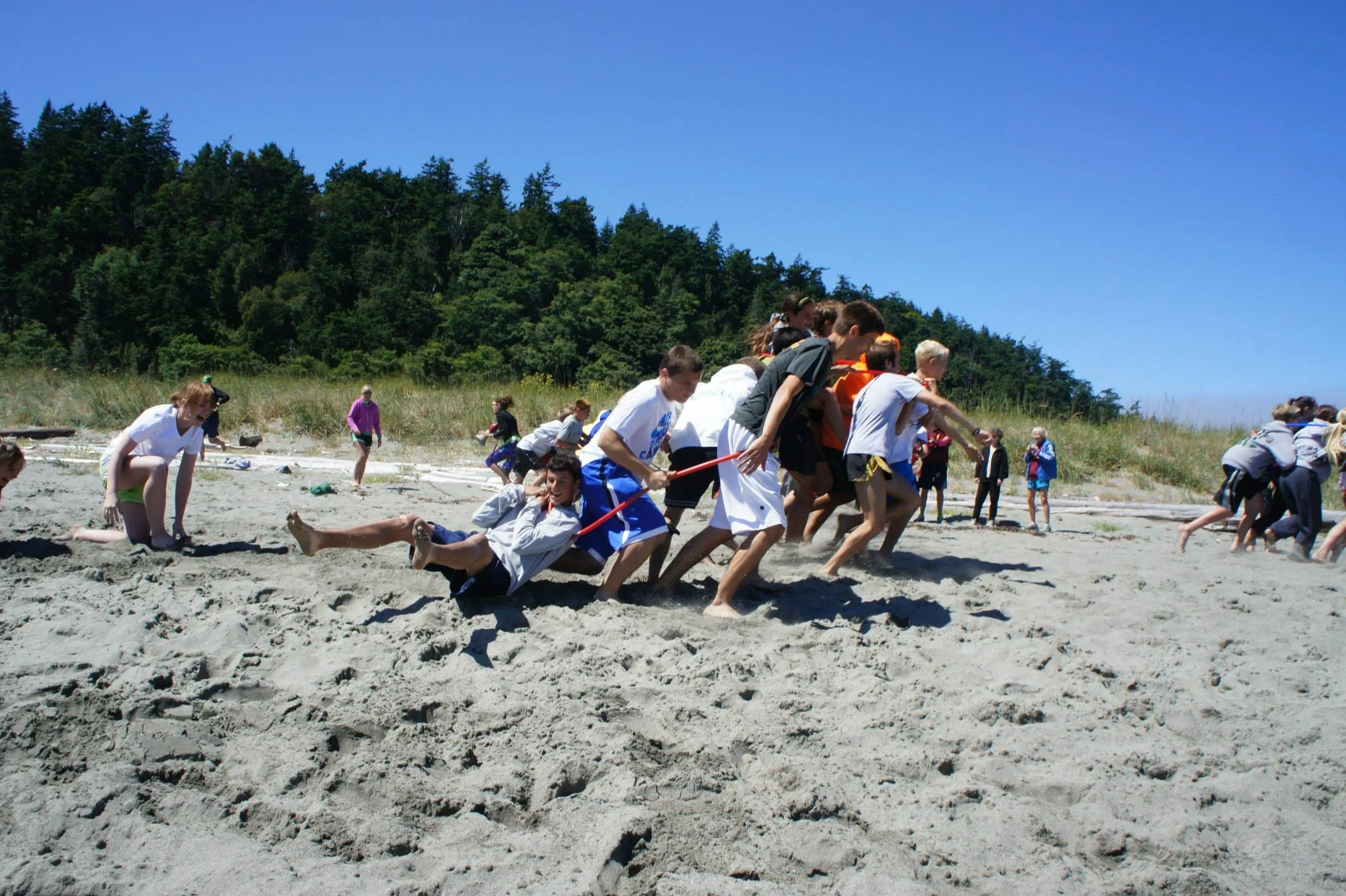 Athletes participating in a tug-of-war game on a sandy beach at Fort Casey Running Camp - Youth Running Camp