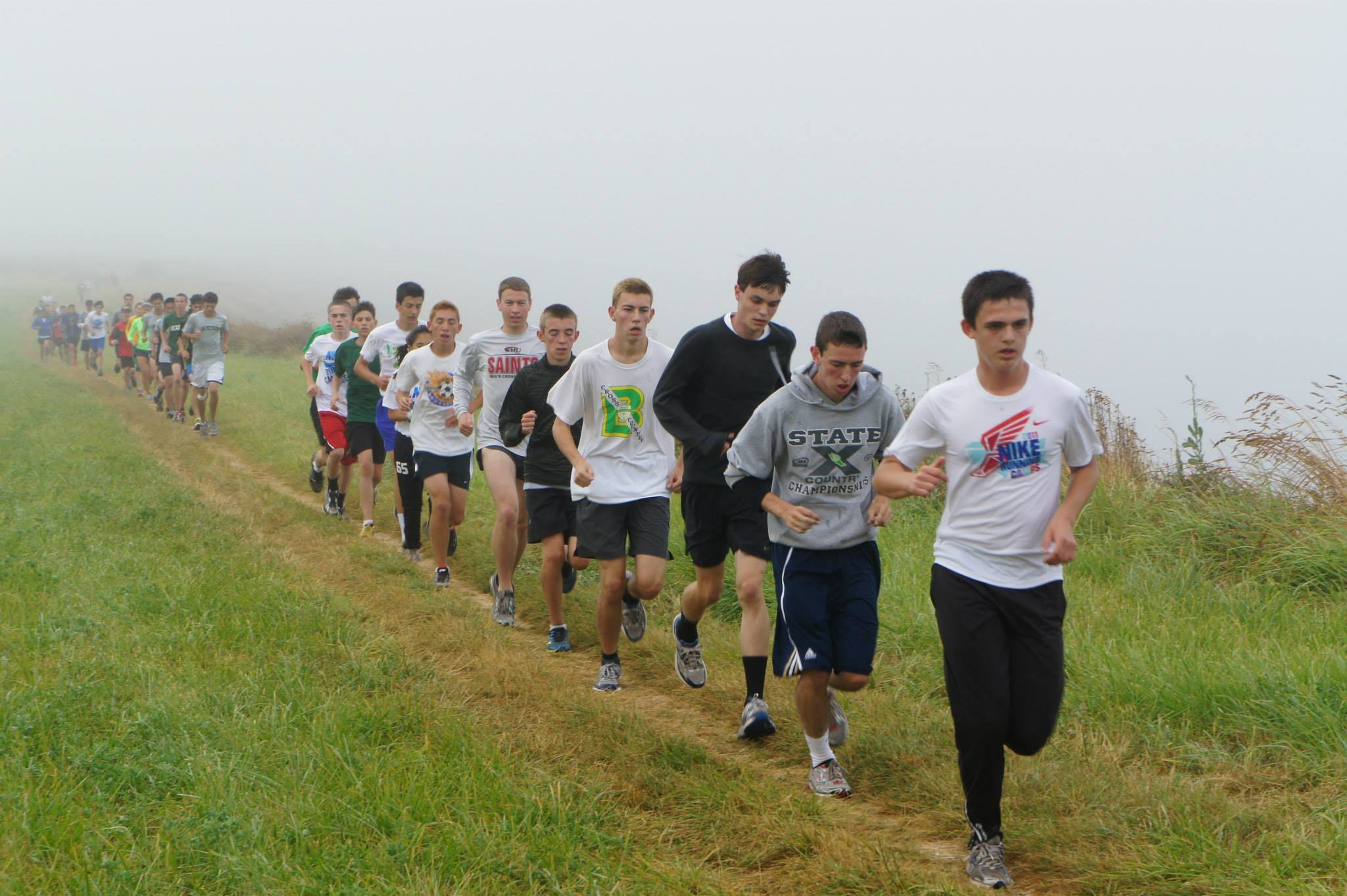 Group of teenagers running on a grassy trail in misty weather at Fort Casey Running Camp - Youth Running Camp