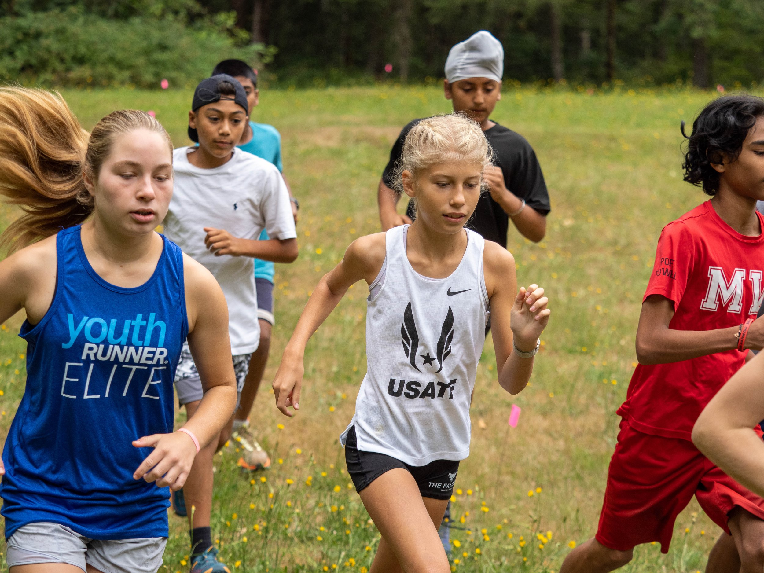 Kids running outdoors in a grassy field with trees in the background, participating in a race or running event at the Elite Middle School Camp at Youth Runner Camps