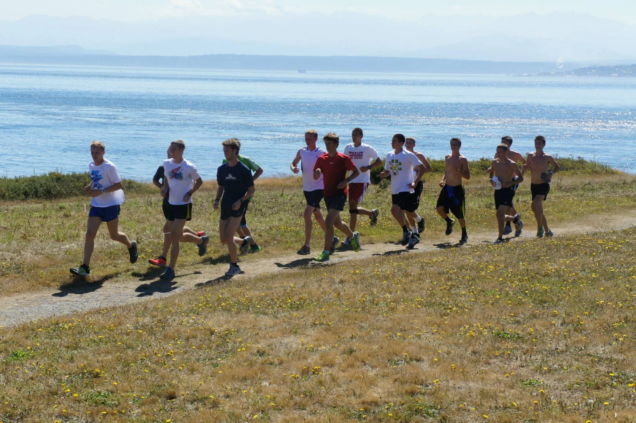A group of teenage boys running along a dirt path on a grassy field at Fort Casey Running Camp - Youth Running Camp